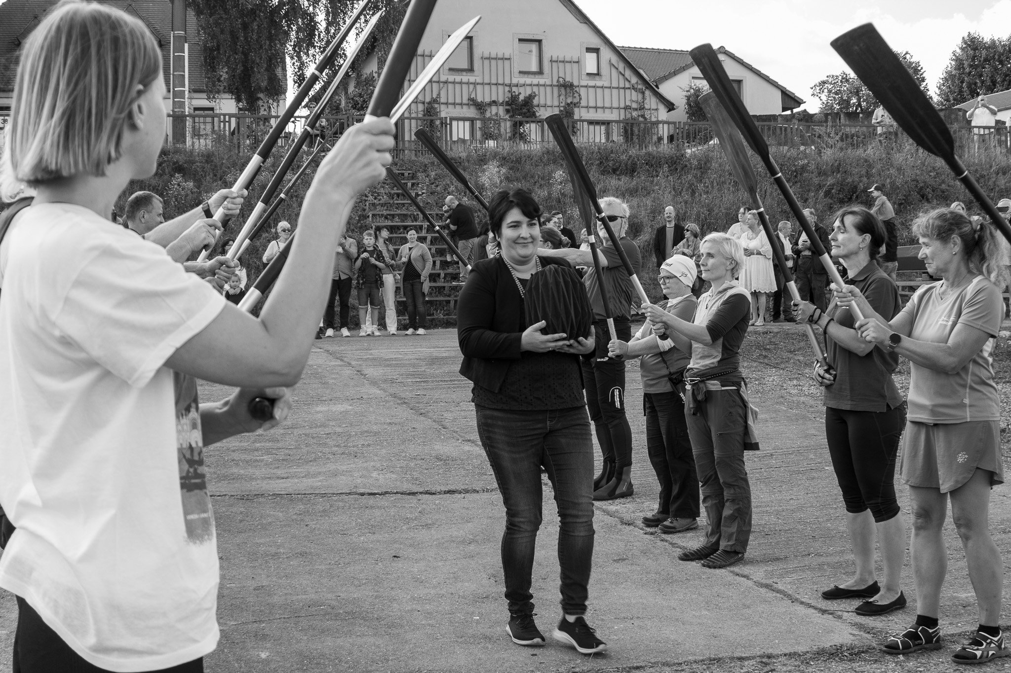 Eine Frau wird beim Empfang eines Preises von mehreren Frauen mit Paddeln in einer Linie auf dem Sportplatz geehrt, während Zuschauer im Hintergrund zuschauen.