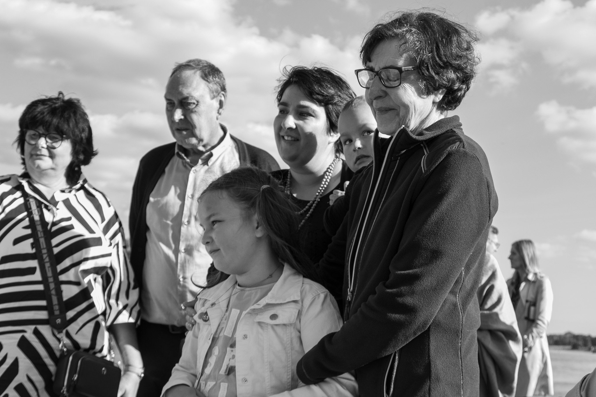 Eine Gruppe von Menschen verschiedenen Alters, einschließlich Kindern, steht im Freien unter einem Himmel mit Wolken.