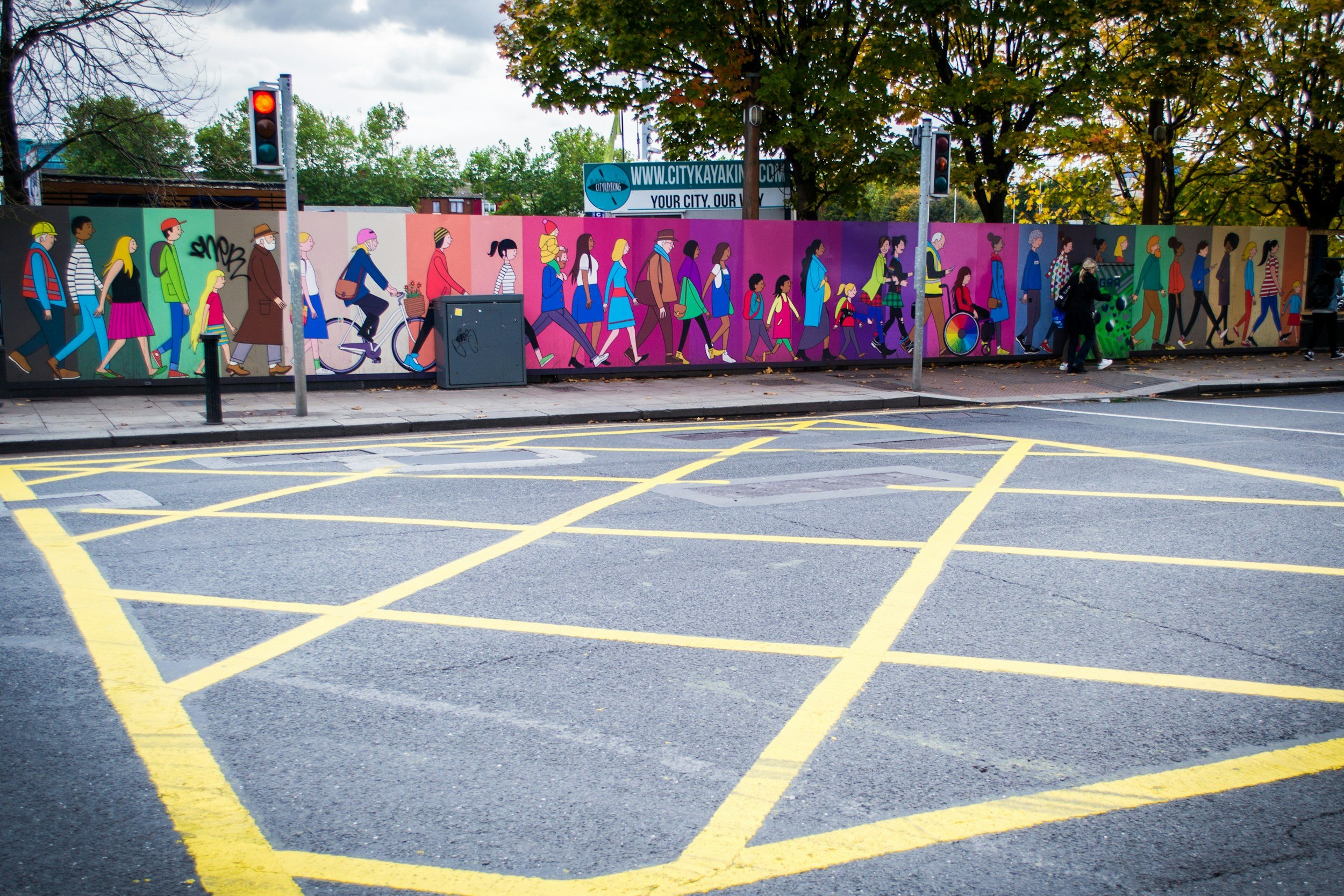 Straßenkunst: Bunte Wandmalerei zeigt eine Gruppe von Menschen mit unterschiedlichen Hintergründen und Mobilität, die gemeinsam vor einem urbanen Hintergrund gehen.
