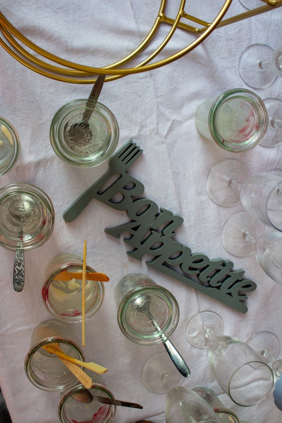 Tischdekoration mit leeren Weingläser, einem „Prost“-Aufleger, kleinen Löffeln, einem silbernen Messer, einem goldfarbenen Teller und einer goldfarbenen Dekoration.