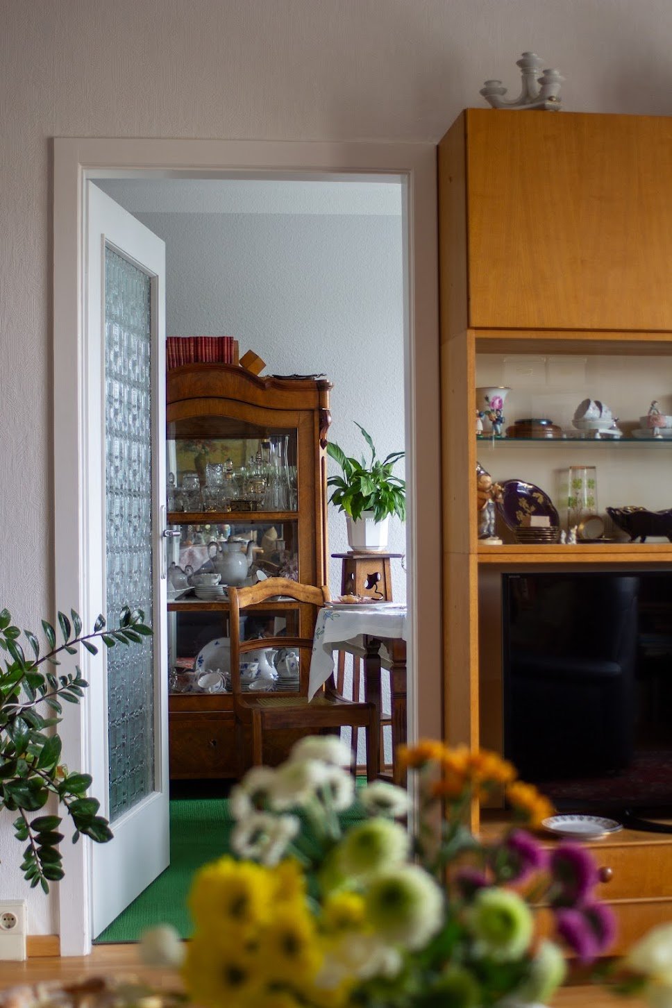 Ein Blick in einen gemütlichen, gut dekorierten Wohnzimmerraum mit einem offenen Blick auf ein Esszimmer im Hintergrund, Möbel aus Holz, Pflanzen und Blumen im Vordergrund.