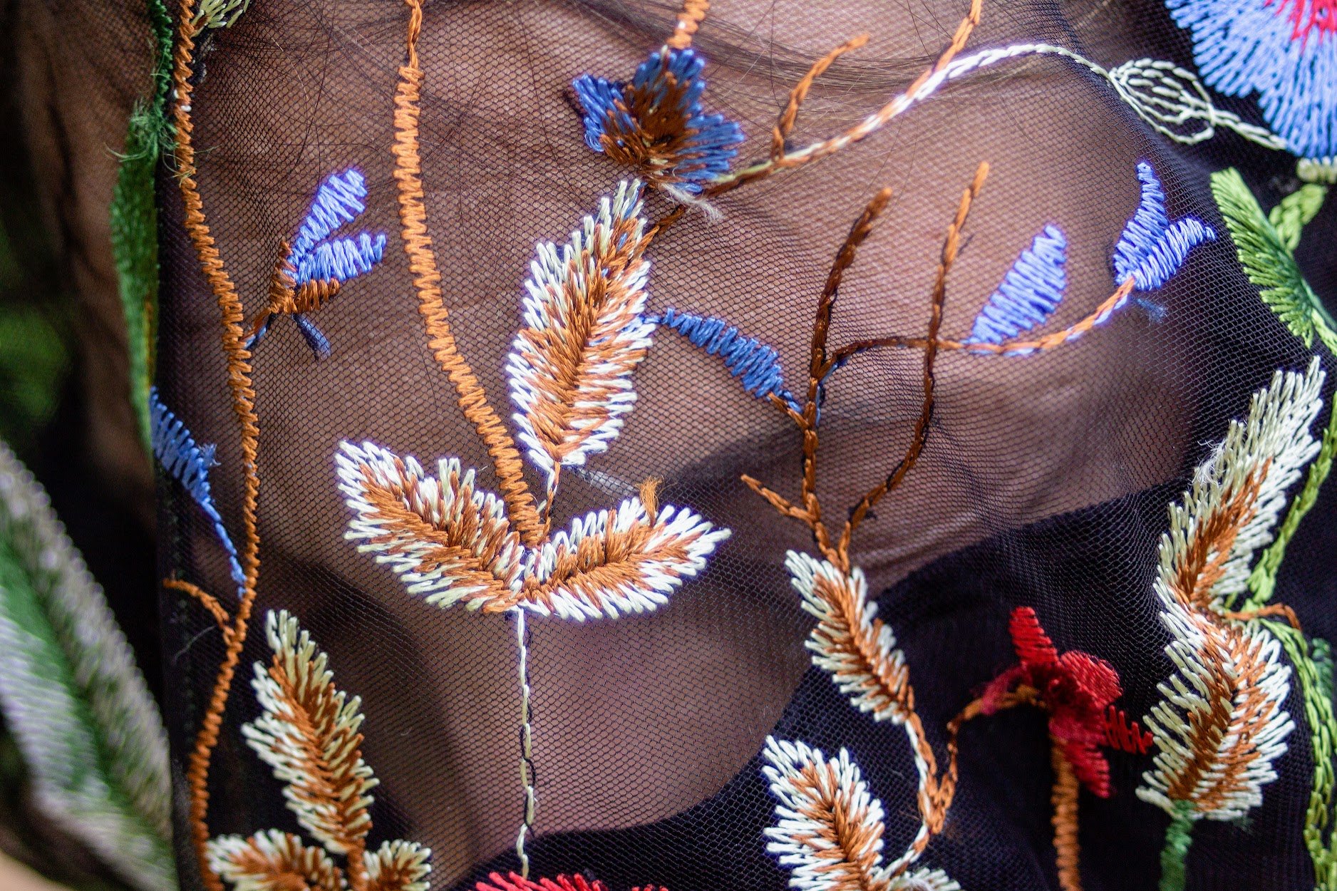 Nahaufnahme eines fein bestickten schwarzen Stoffes mit bunten, hübschen Blüten- und Pflanzenmotiven aus dünnen Garnen.