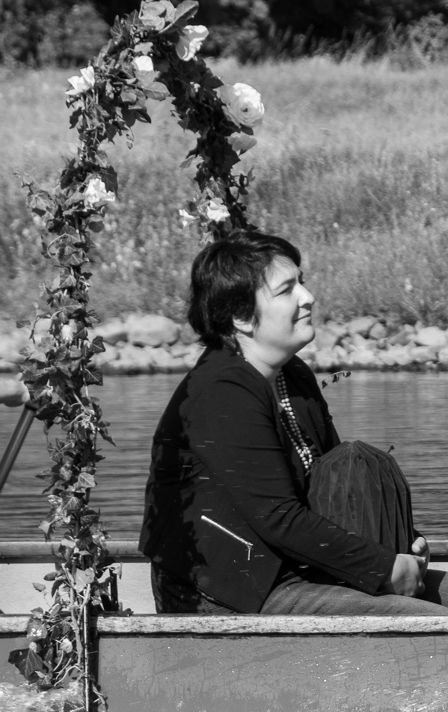 Frau sitzt in einem Boot, umgeben von Wasser, mit einer Blumen-Arrangements oberhalb ihres Kopfes, im schwarzen und weißen Bild.