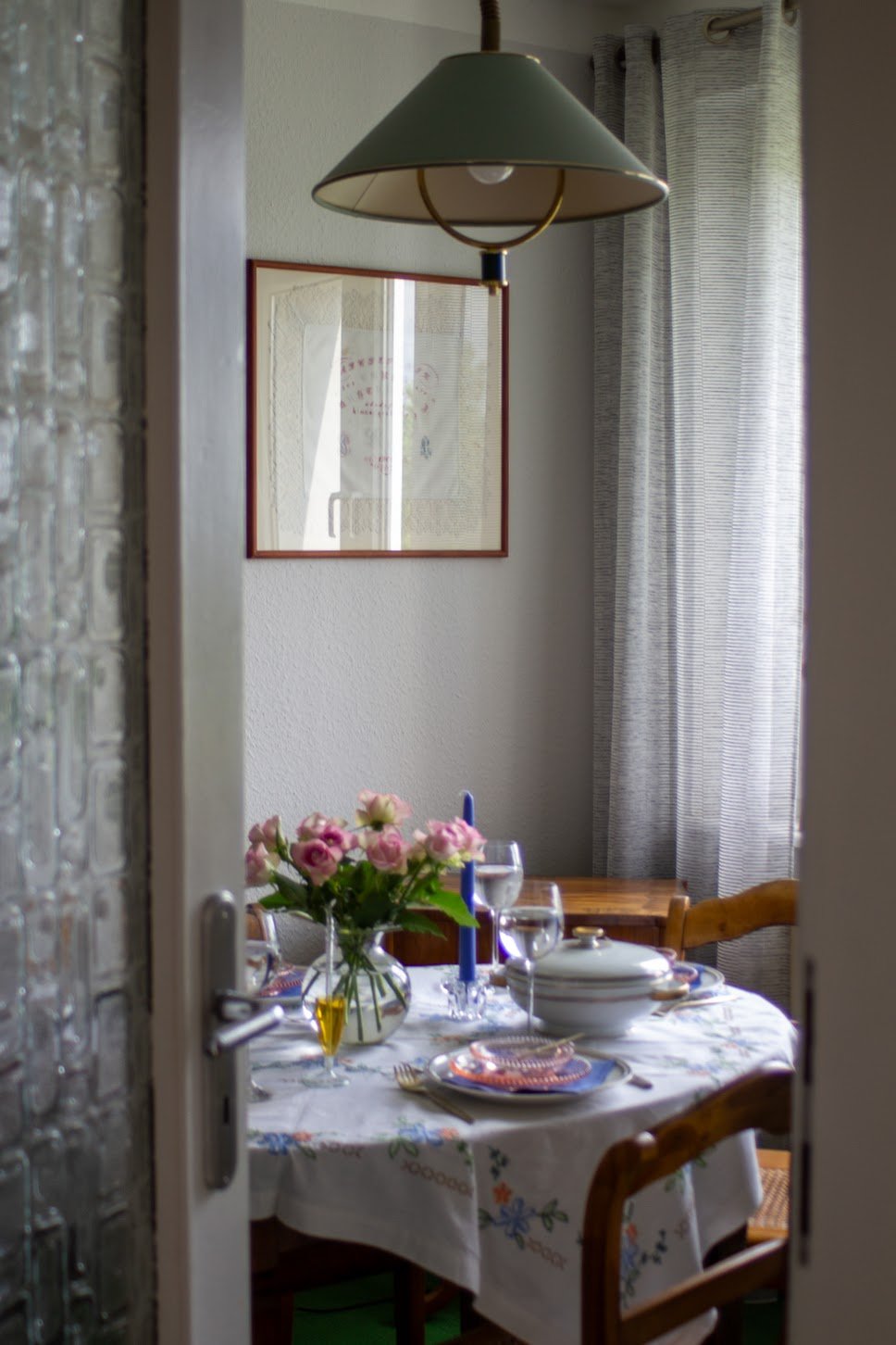 Ein schön gedeckter Tisch in einem Esszimmer, mit Blumenstrauß, Kerzen, Geschirr und Gläser, Blick durch die Türöffnung.