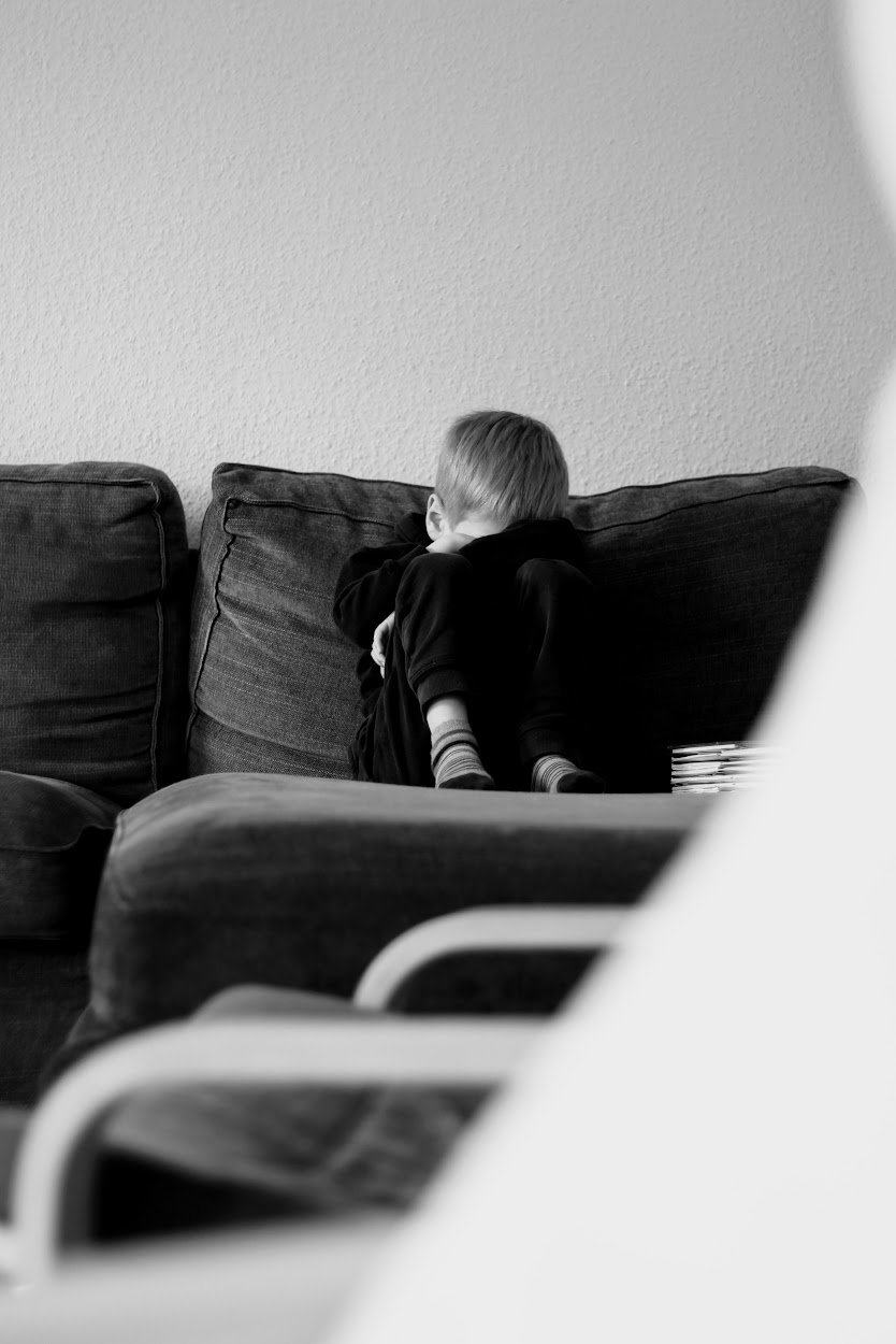Ein Kind sitzt auf einem dunklen Sofa in einer Ecke des Zimmers.
