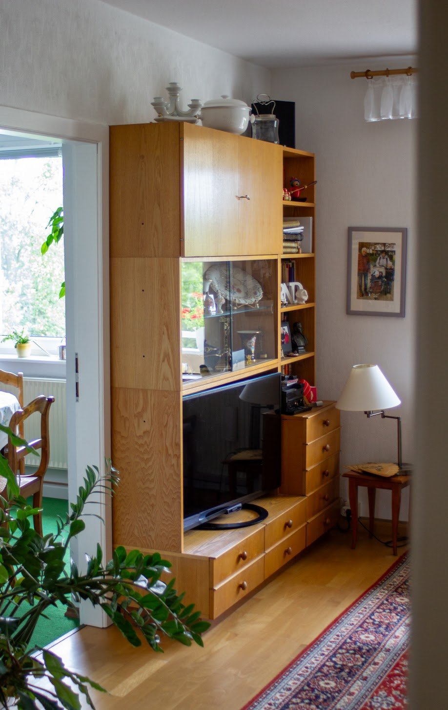 Wohnzimmer mit Holzmöbeln, Fernseher, Stehlampe, Wandbild und Blick in den Wintergarten