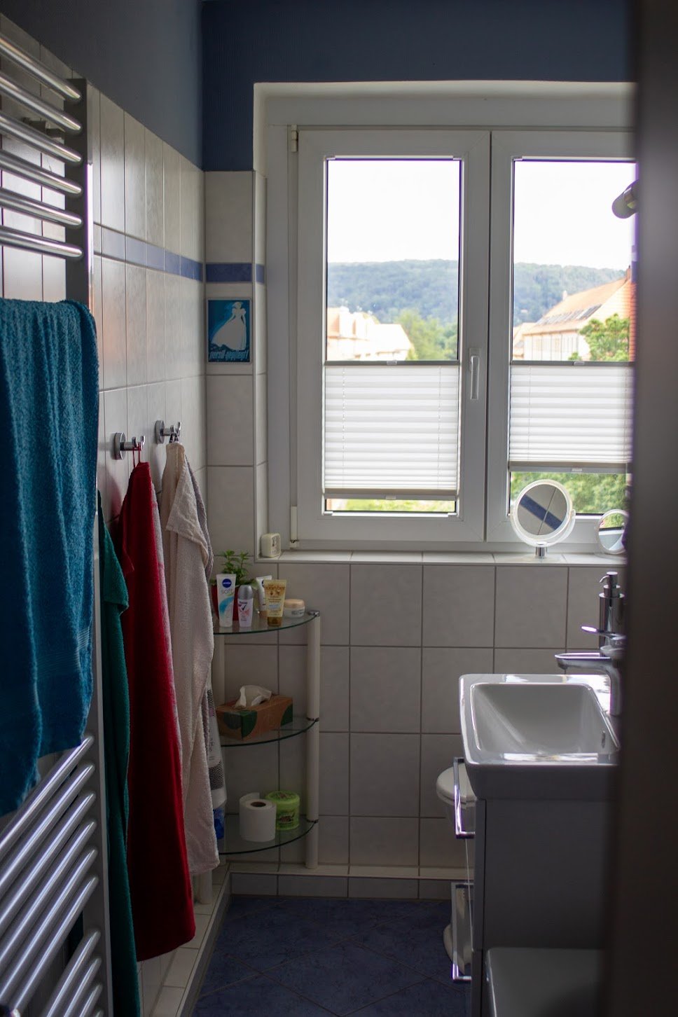 Badezimmer mit Fenster, Handtüchern, Badutensilien und Spiegel