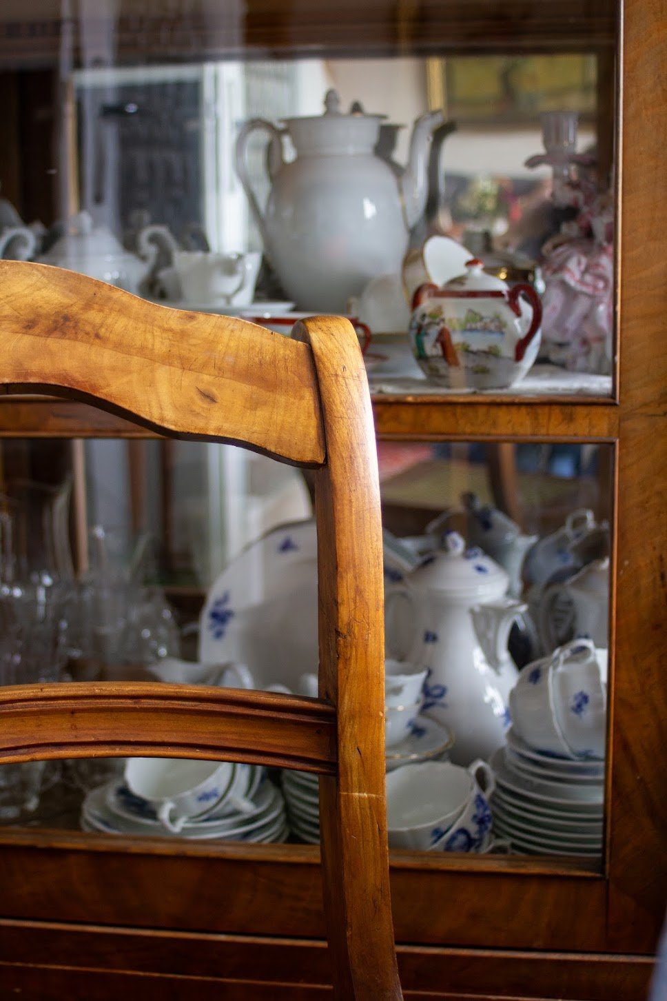Ein antiker Holztisch und eine Glasschrank mit Porzellan-Teekannen, Tassen und Tellern im Vintage-Stil.