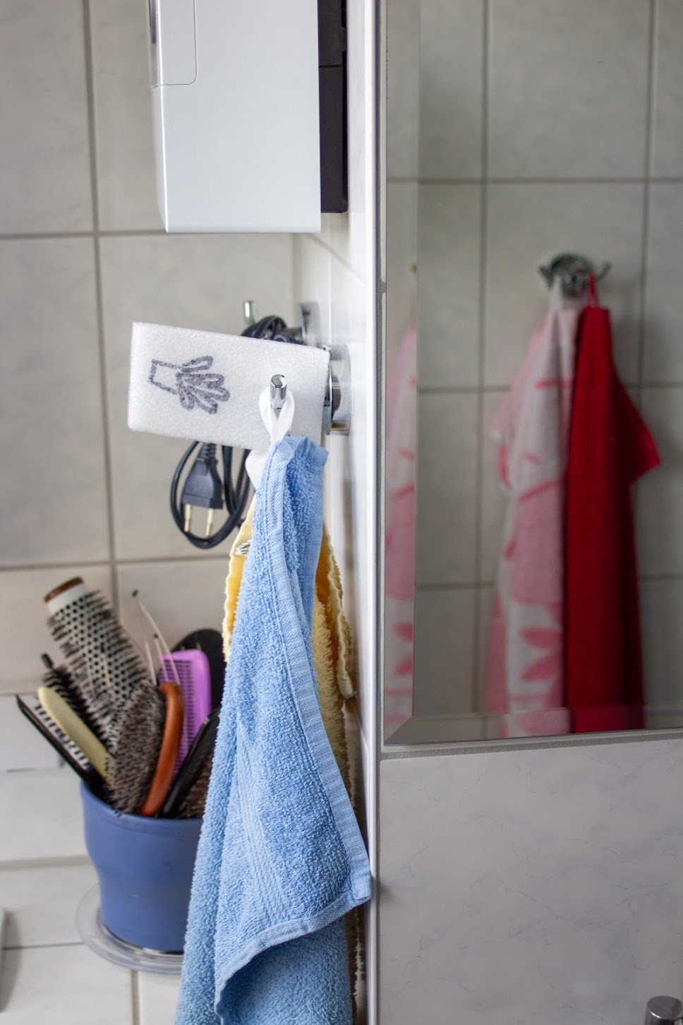 Badezimmer mit Handtüchern, Haarkämme, Haargummis und Waschutensilien. Handtücher hängen an einer Wandhalterung, und es gibt eine Spiegelseite mit weiteren Handtüchern.