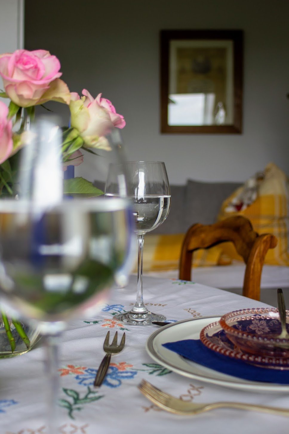 Ein gedeckter Esstisch mit Blumen, Wein, Besteck und Geschirr in einem Wohnzimmer