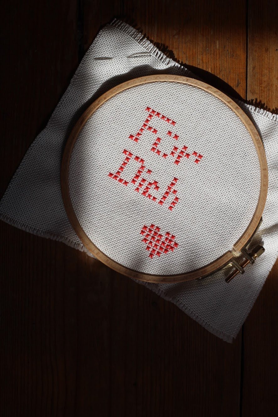 Stickrahmen mit einem Kreuzstich-Motiv, das ein Herz und das Wort 'LOVE' bildet.