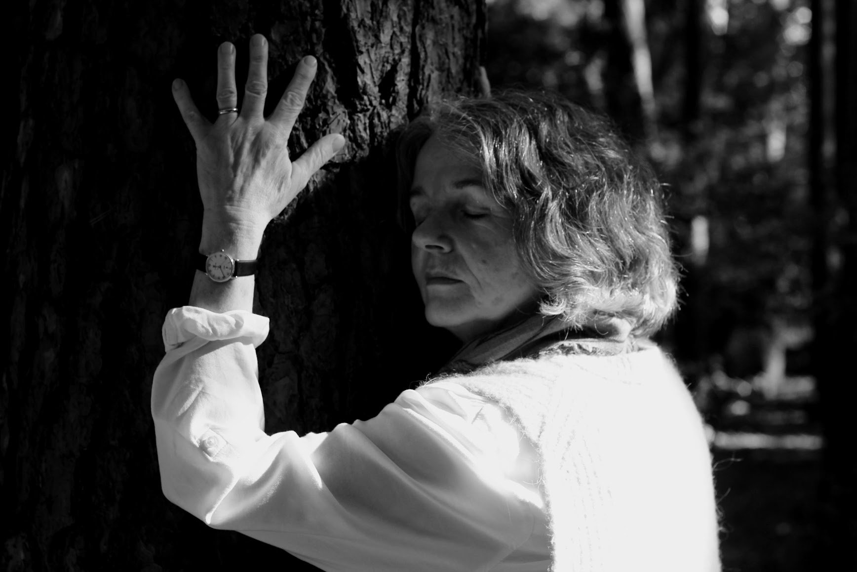 Eine Frau mit geschlossenem Blick lehnt sich an einen Baum im Wald, in Schwarz-Weiß-Fotografie.