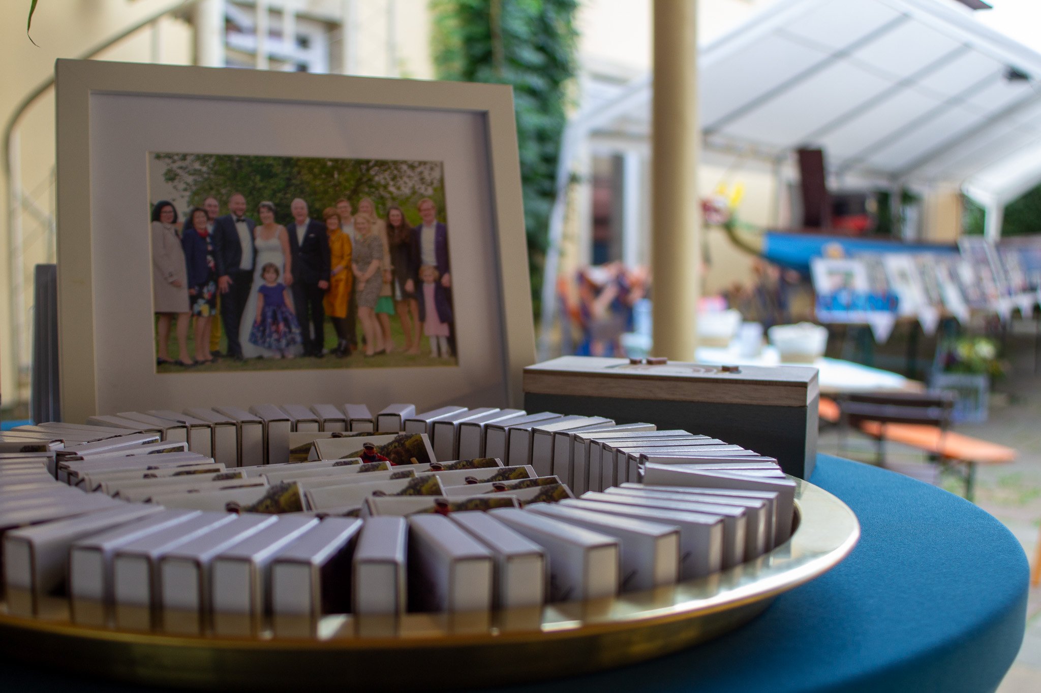 Ein gerahmtes Familienfoto, ein Ring aus kleinen Schokoladentäfelchen und ein Päckchen auf einem blauen Tisch in einem Zelt bei einer Feier