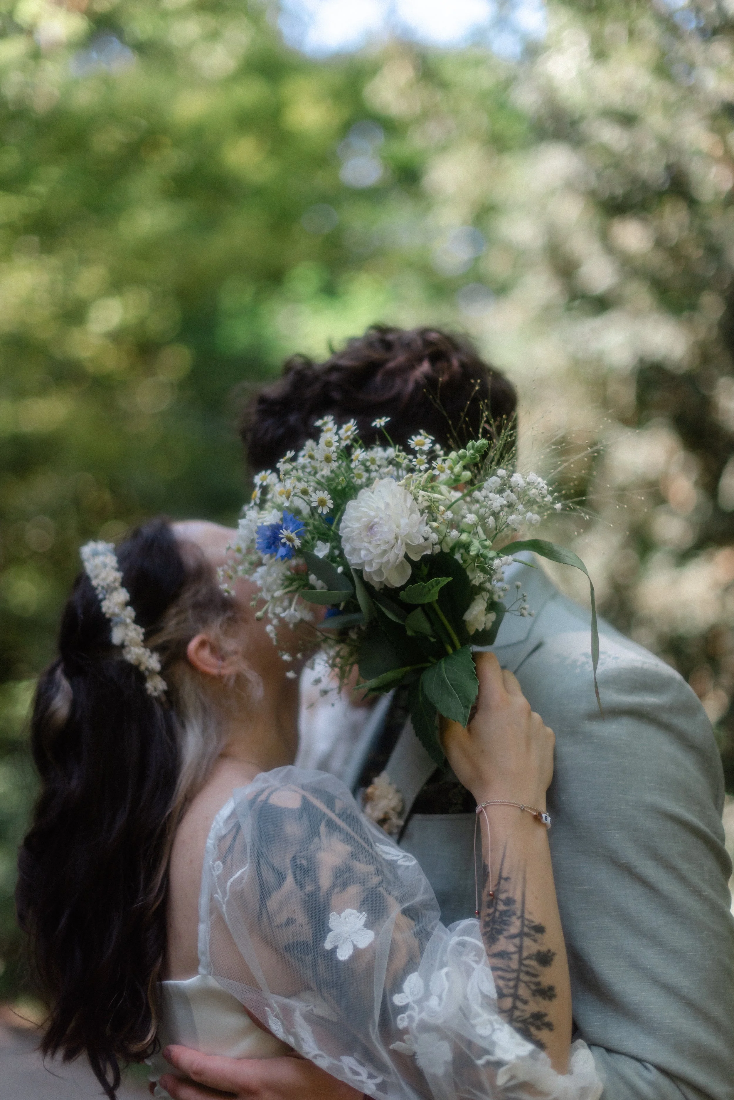 Ein Brautpaar bei einer Hochzeit im Freien, die Braut hält einen Blumenstrauß, sie trägt ein weißes Kleid und einen Blumenkranz im Haar, der Bräutigam trägt einen Anzug.