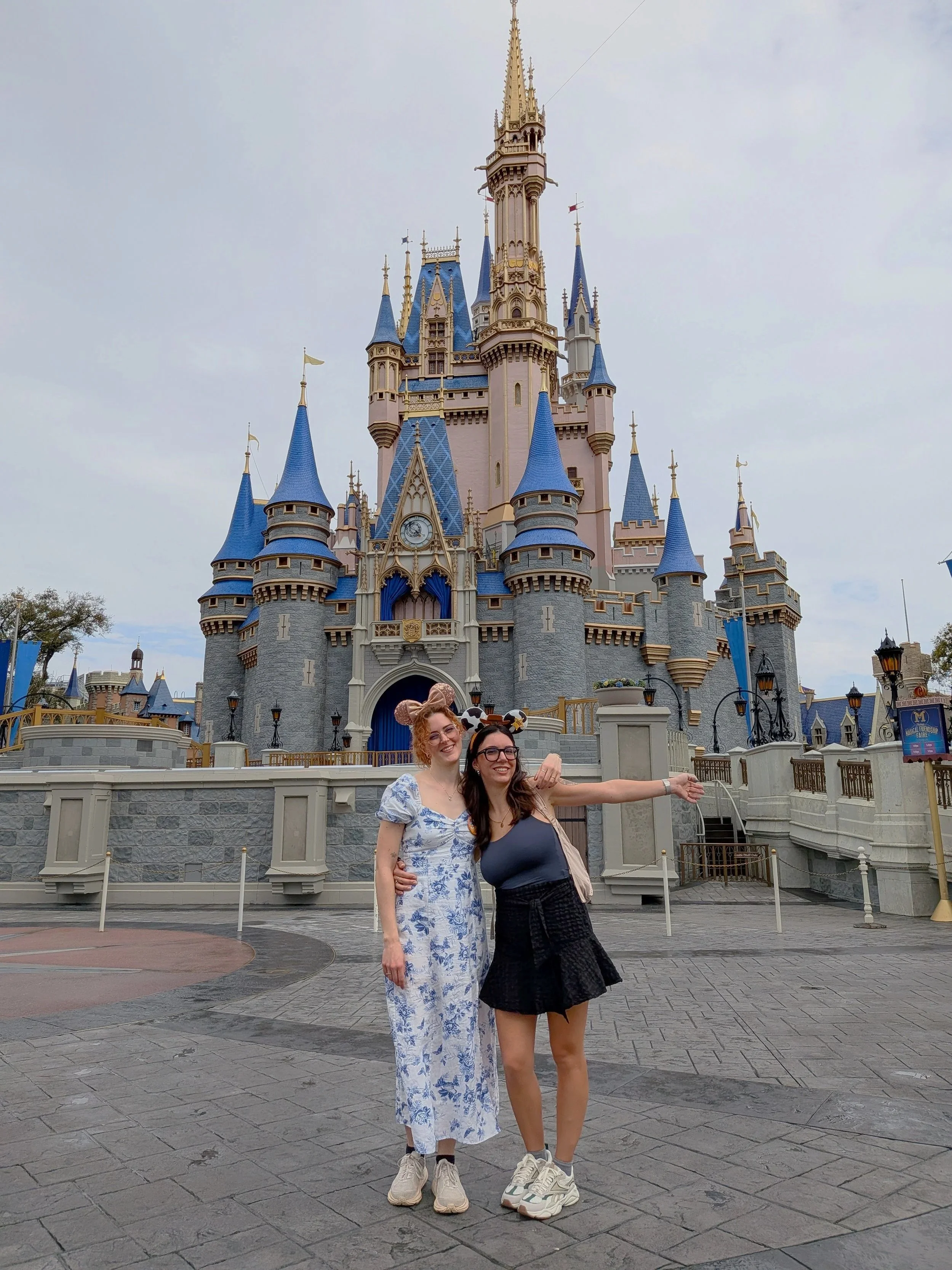 Zwei Frauen posieren vor dem Cinderella-Schloss in Disneyland, beide tragen Mickey Mouse Ohren und lachen.