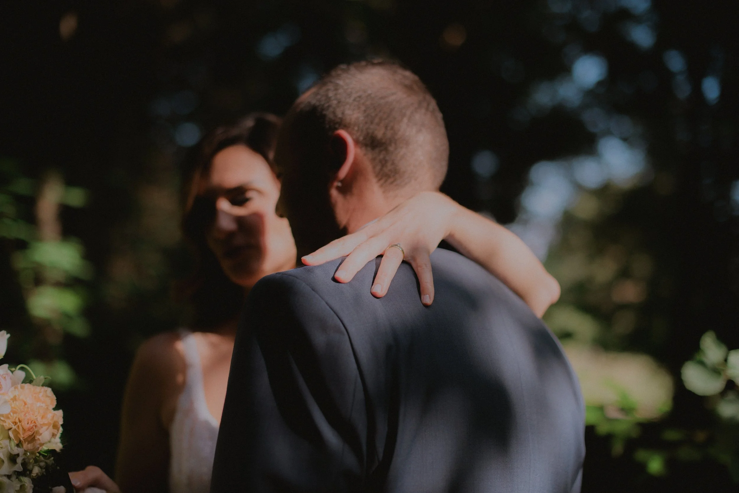 Ein Paar bei einer romantischen Begegnung im Freien, vermutlich bei einer Hochzeit, mit Fokus auf den Armen und Schultern der beiden Personen, während sie sich nahe stehen.