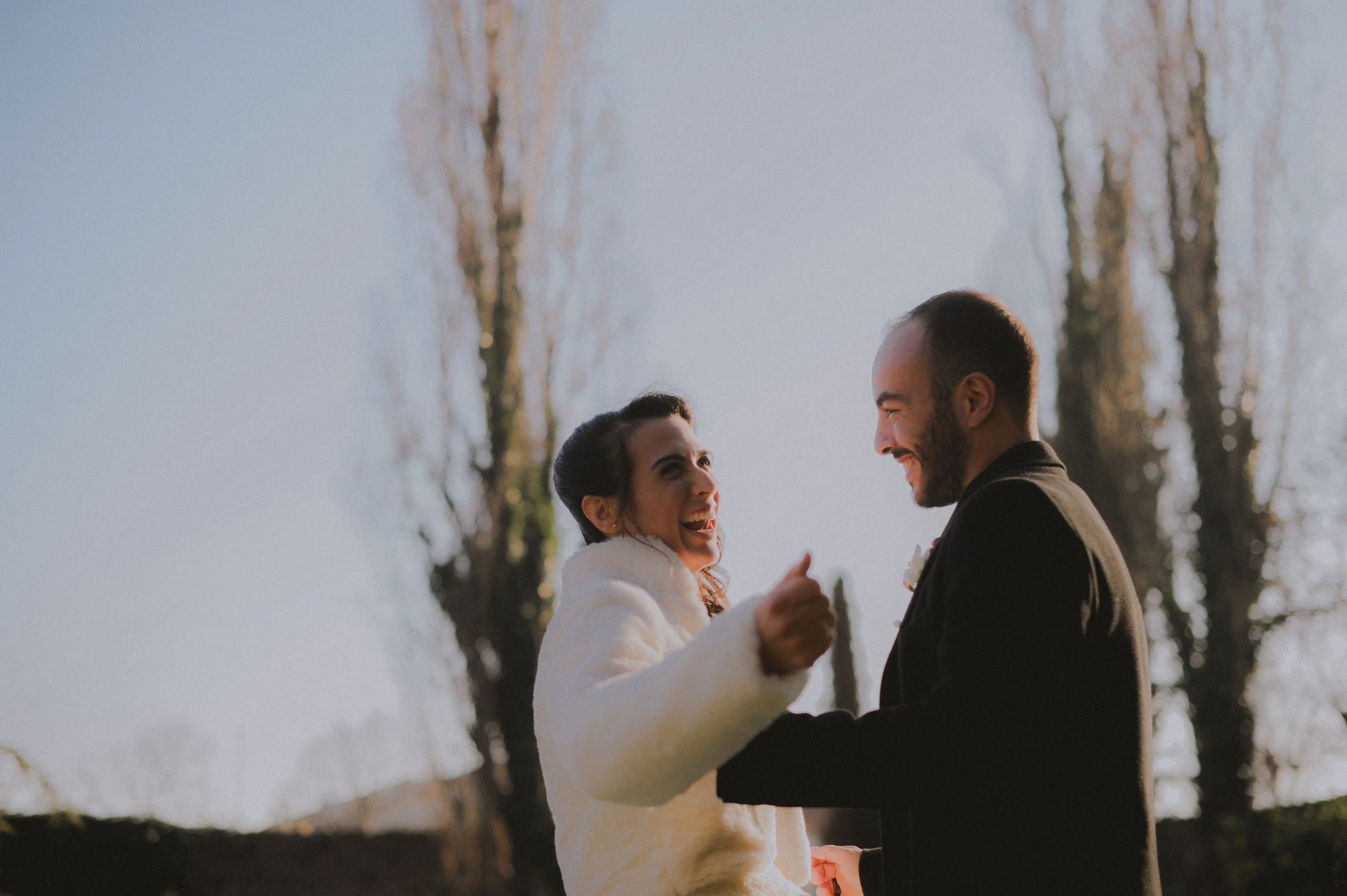 Ein Paar bei einer Hochzeit, lachend und Händchen haltend im Freien bei Sonnenuntergang.