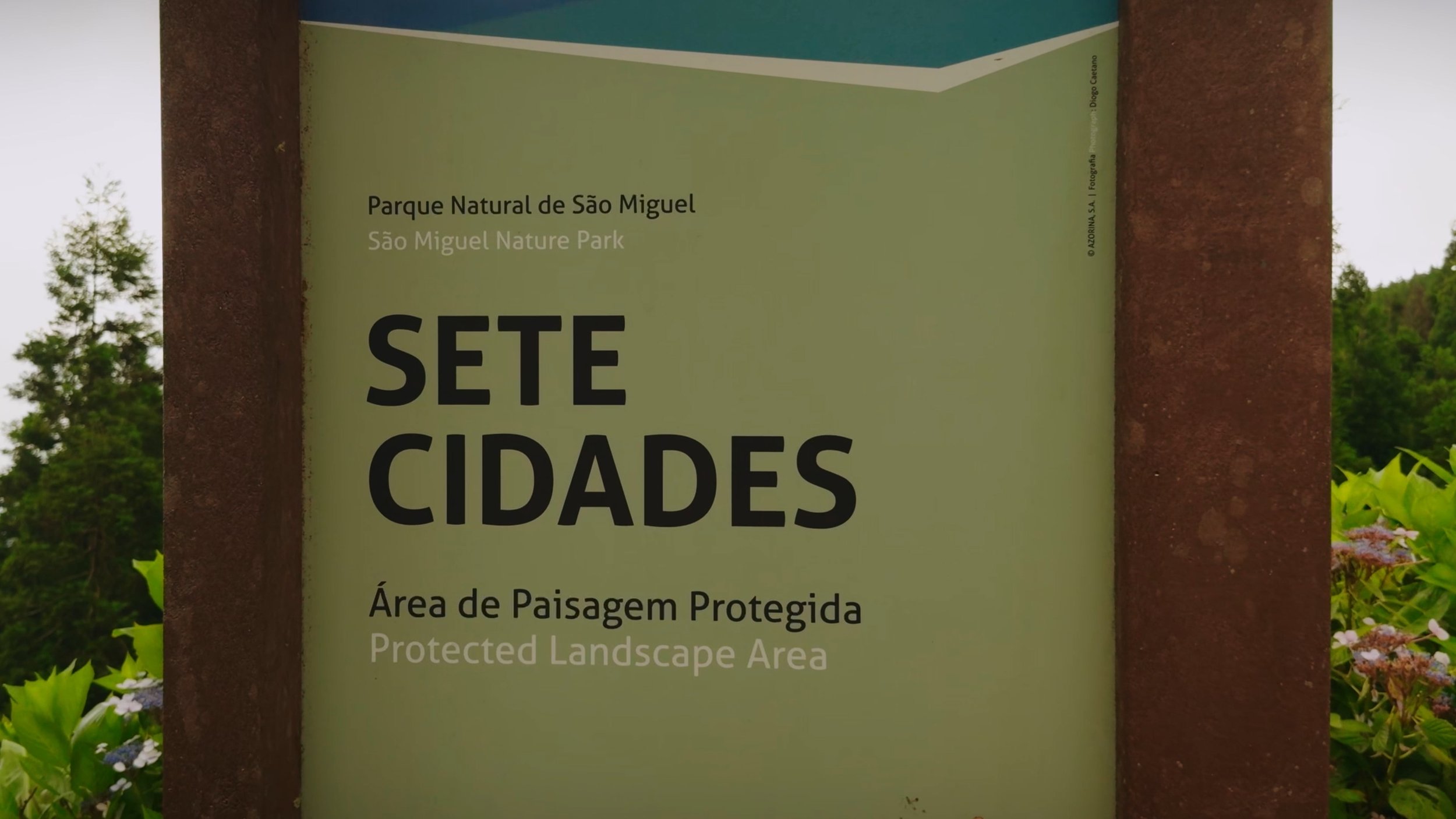 Signboard at São Miguel Nature Park indicating it is a protected landscape area in Portuguese and English, with trees and greenery in the background.