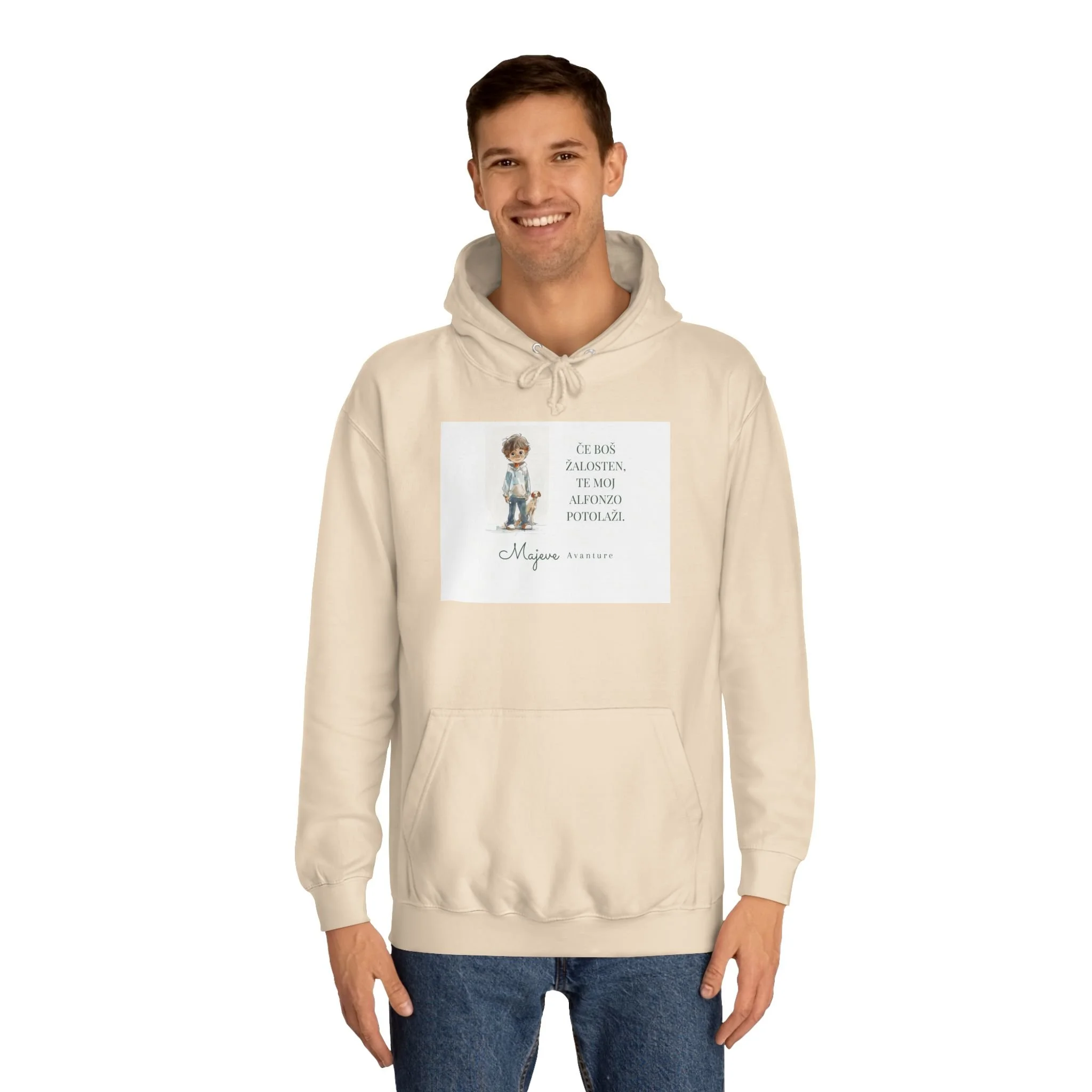 A young man wearing a beige hoodie with a printed illustration and text, smiling, against a white background.
