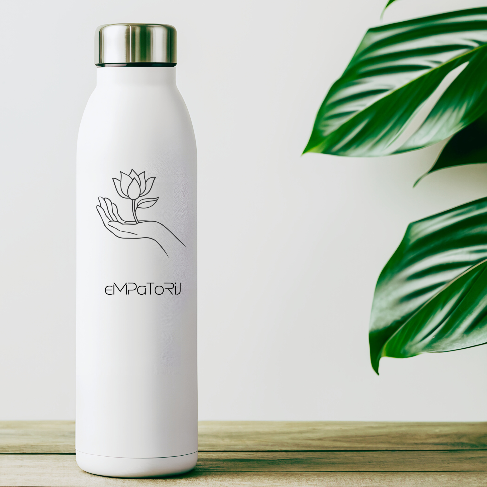 A white insulated water bottle with a silver cap, featuring a minimalist line drawing of a hand holding a blooming flower, with the text 'eMPaTORi' below the image, positioned on a wooden surface with green leaves partially visible on the right.