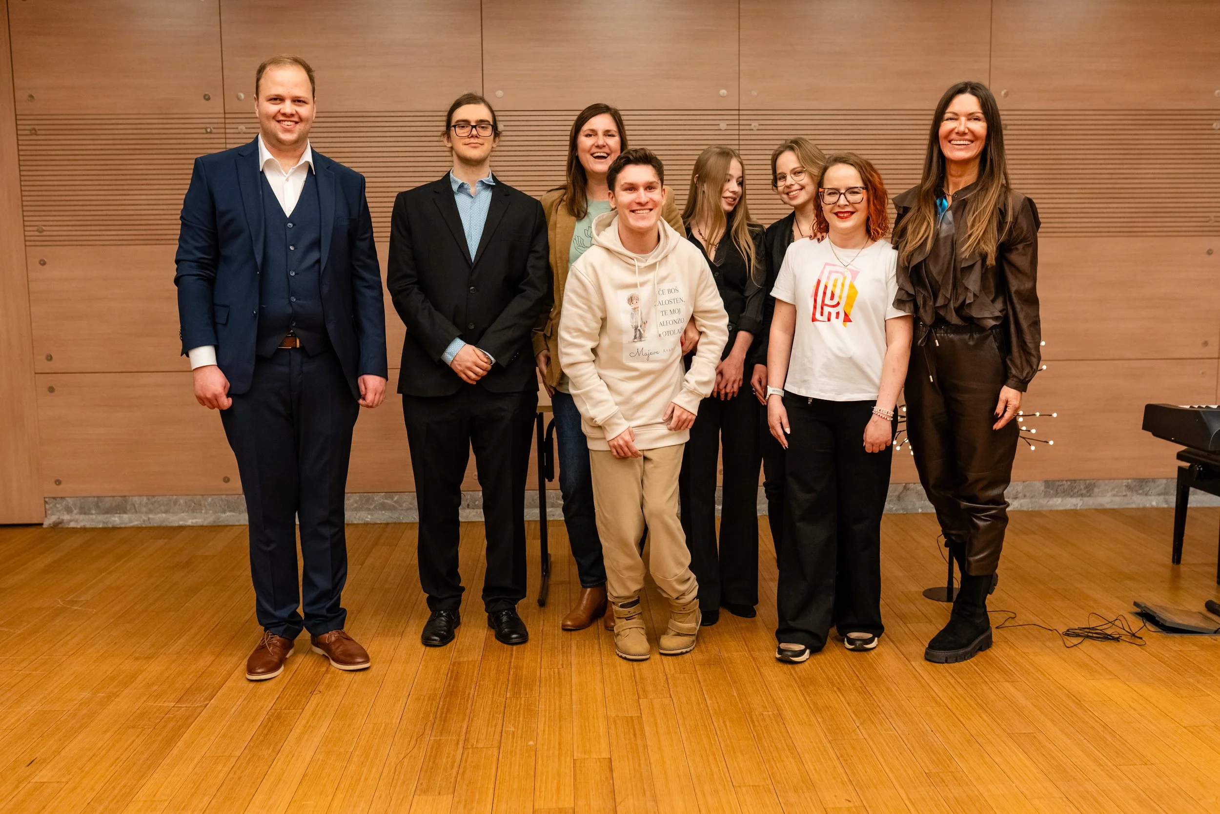 Group of eight people standing together in a row indoors, posing for a photo with a wooden wall background.