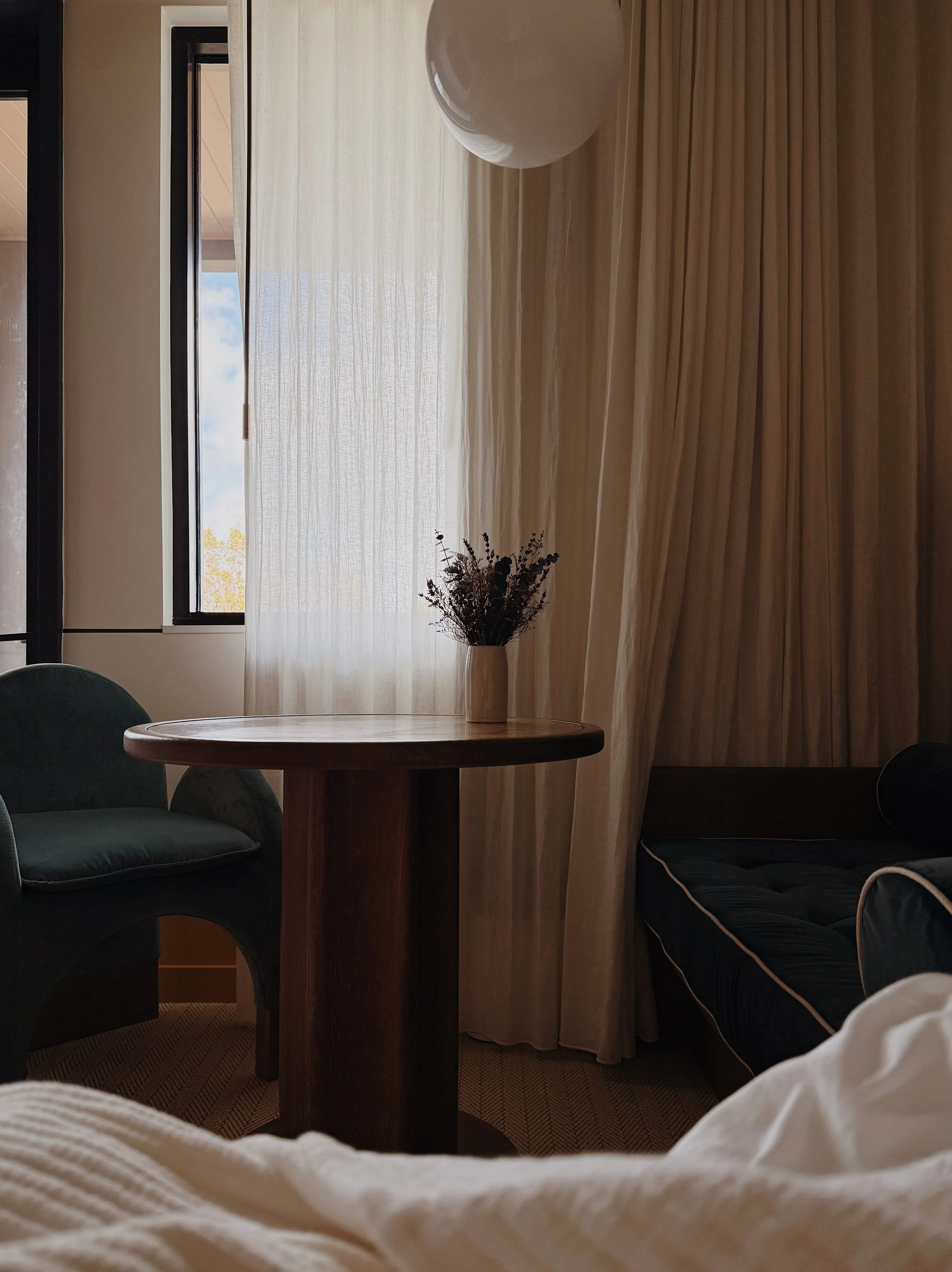 Guest room detail at Hotel Henrietta in New Orleans, featuring soft natural light, textured curtains, and sculptural bedside table.