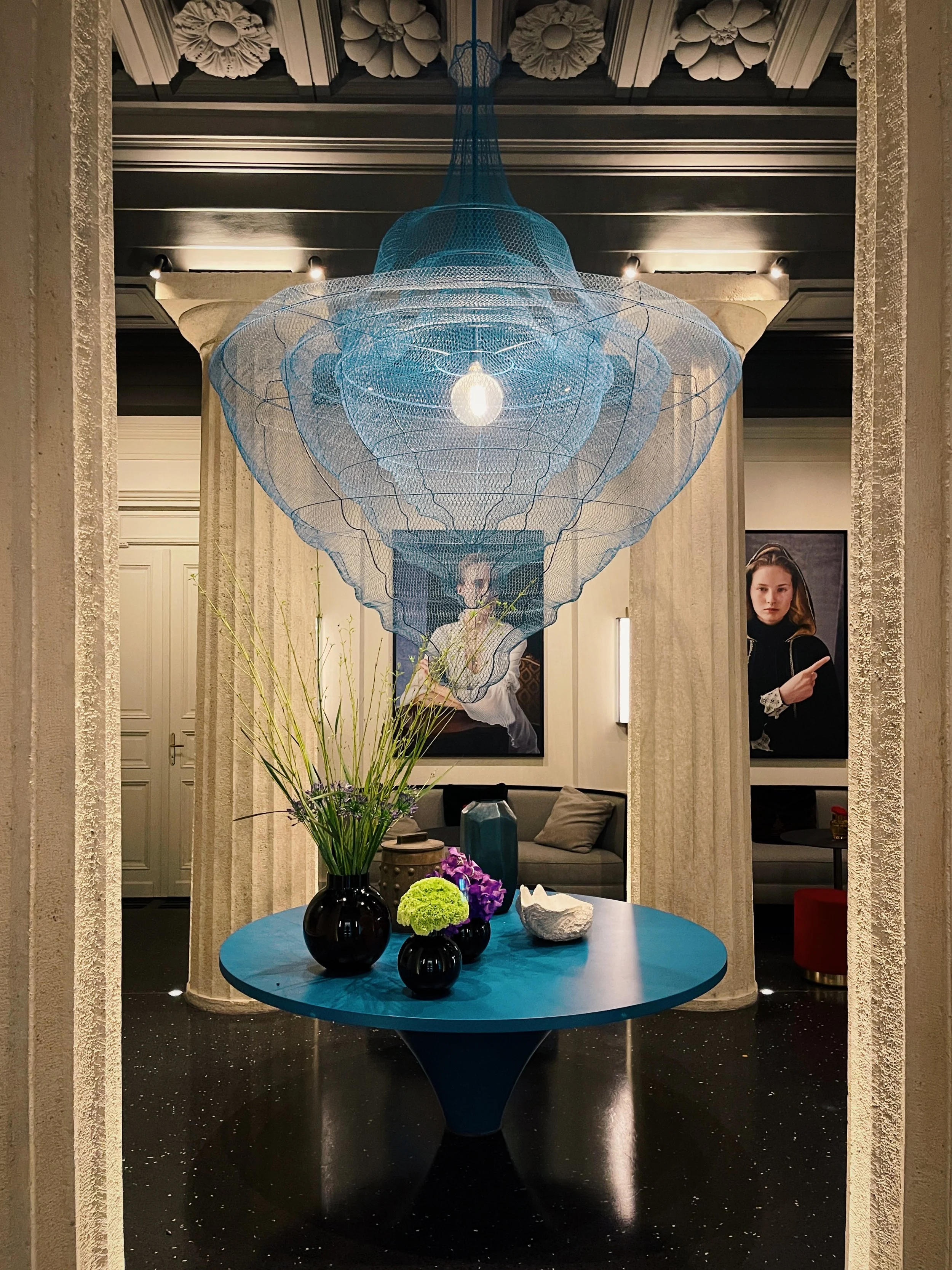 Lobby interior at Dorothea Hotel in Budapest, featuring sculptural blue chandelier and classical architectural columns.