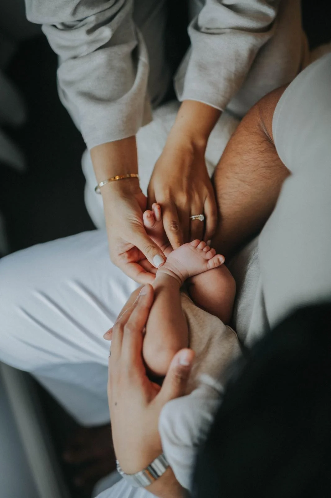 A person holds a baby's foot, with another person's hand gently touching the baby's toes, inside an airplane or similar setting.