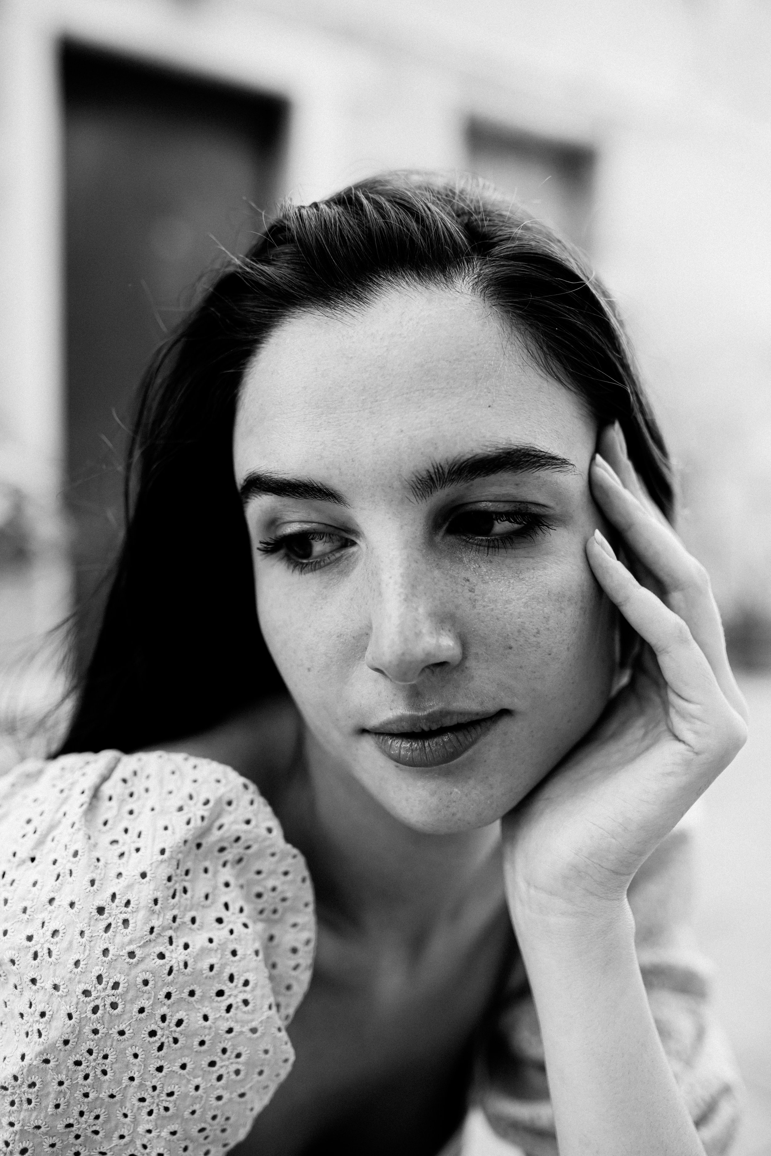 Primo piano di una donna con capelli lunghi e scuri, che guarda verso il basso, mano sulla guancia. Immagine in bianco e nero.