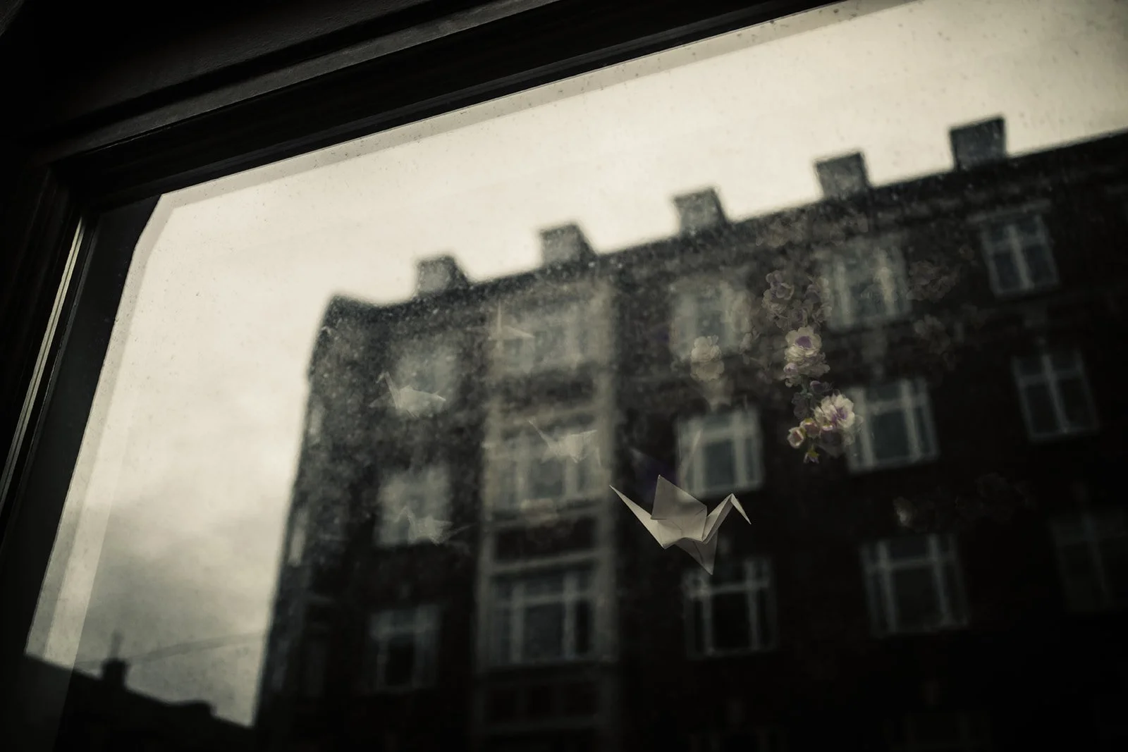 Una finestra con una carta di carta formato origami attaccata alla superficie del vetro, con una scena di un edificio di più piani con finestre in background