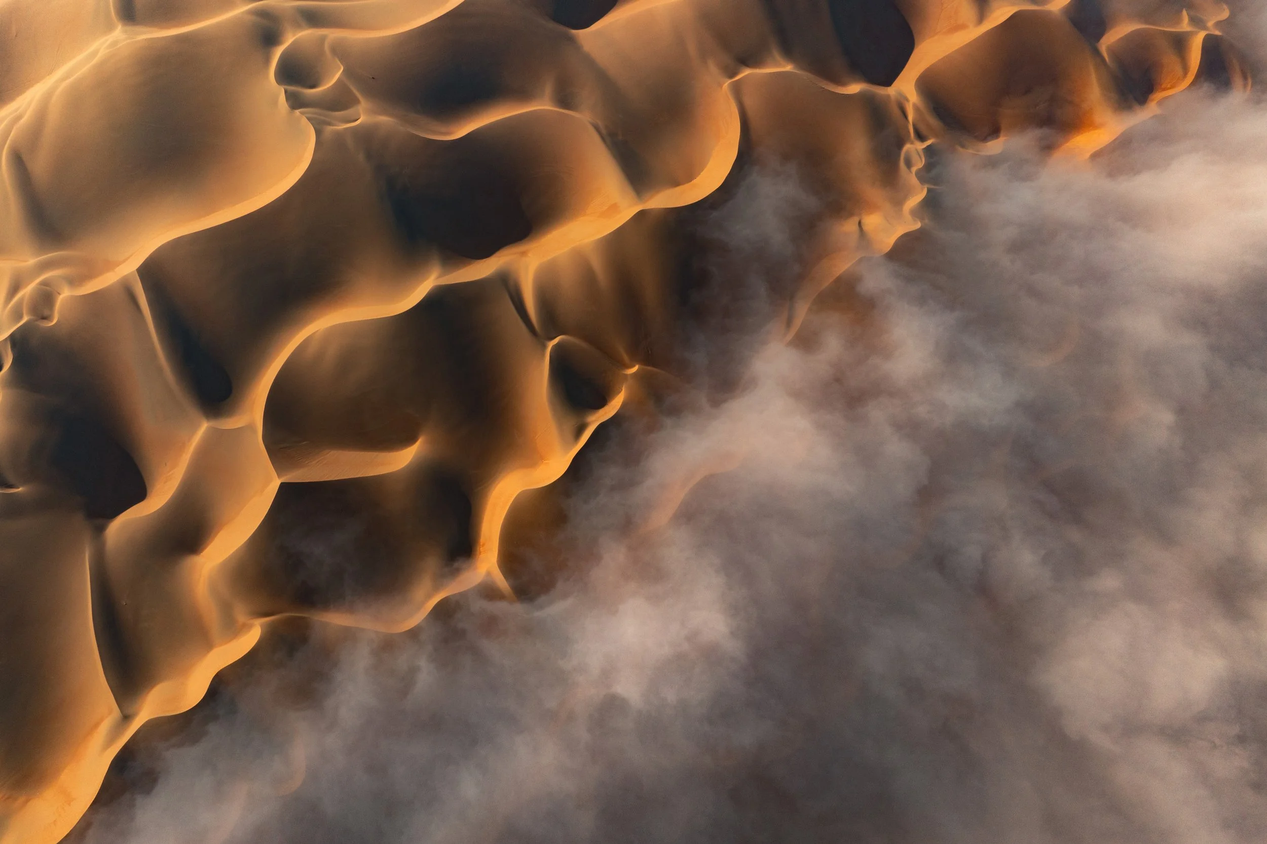 Aerial view of sand dunes with smooth, undulating shapes and a misty atmosphere in Abu Dhabi Desert, the empty quarter - photograph by Khalid Alhammadi, SARAB Art Production