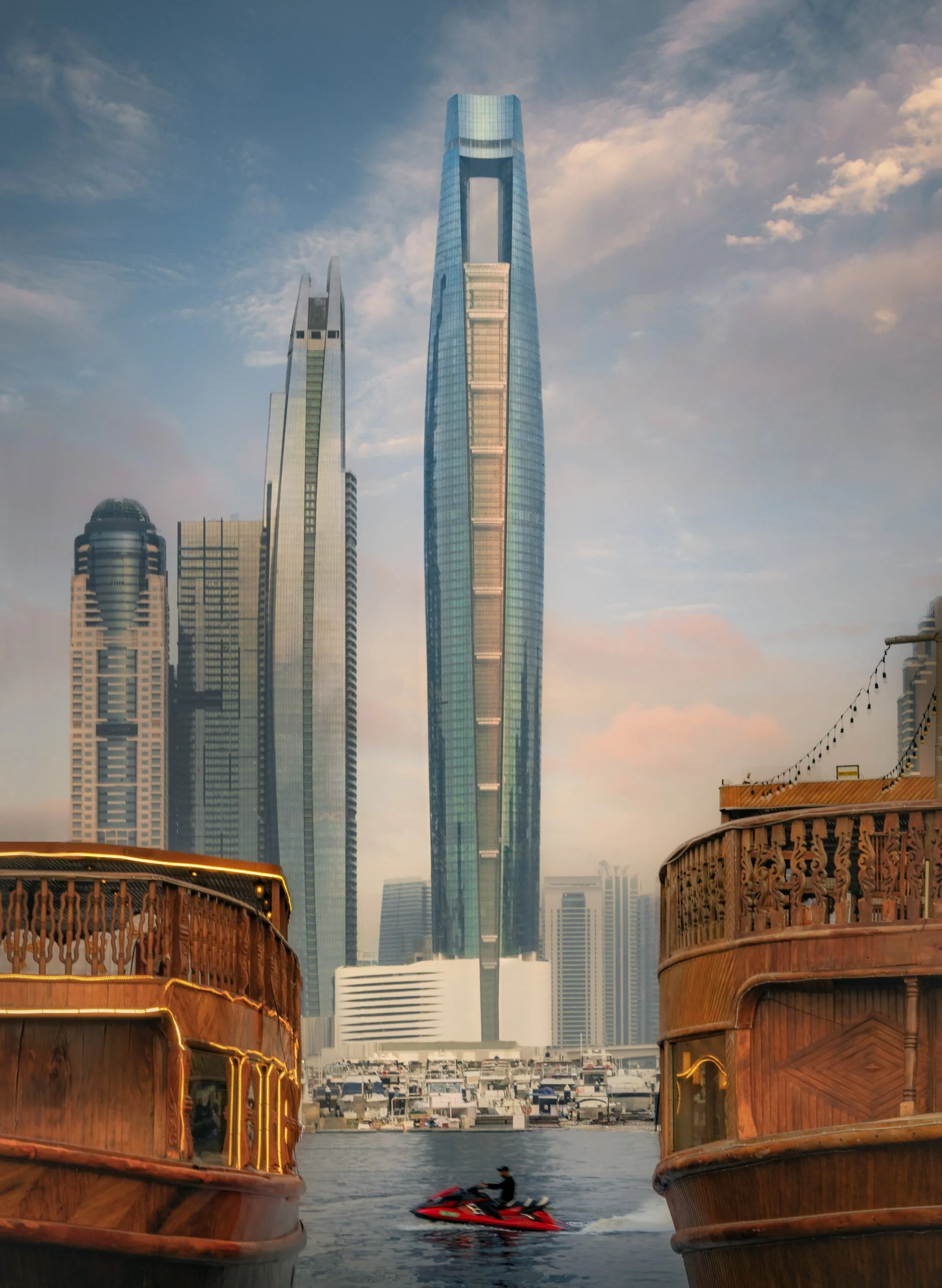 Ciel Dubai Marina framed between the sterns of two wooden dhows, a jet ski crossing the channel.