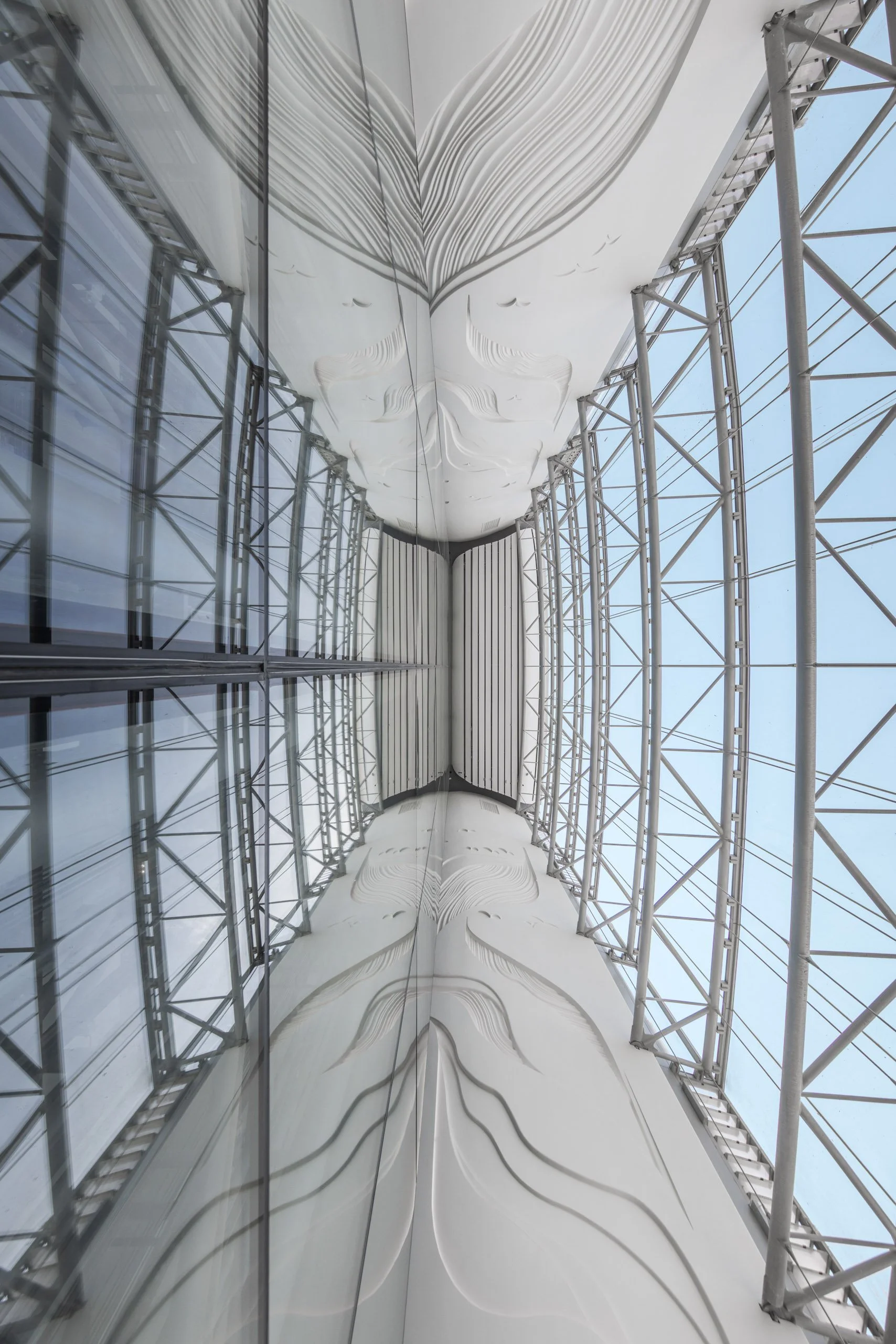 Looking up at a modern building's exterior with reflective glass and white decorative panels, supported by metal scaffolding.
