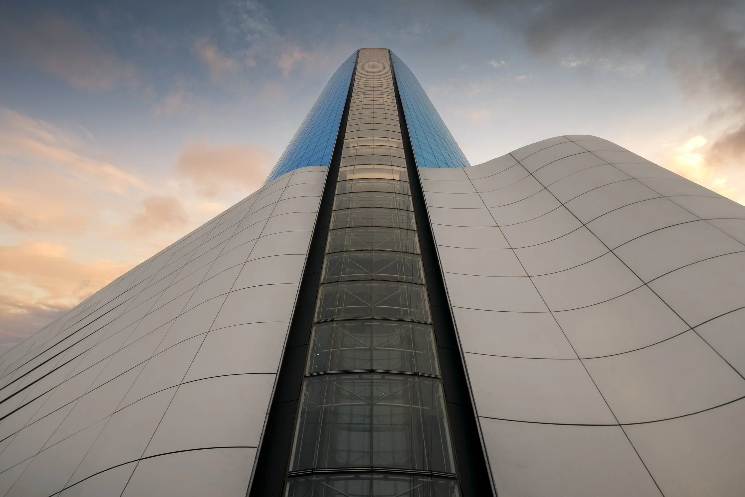 Looking up the glazed slot in the podium of Ciel Dubai Marina at dusk, the tower rising beyond the white cladding.