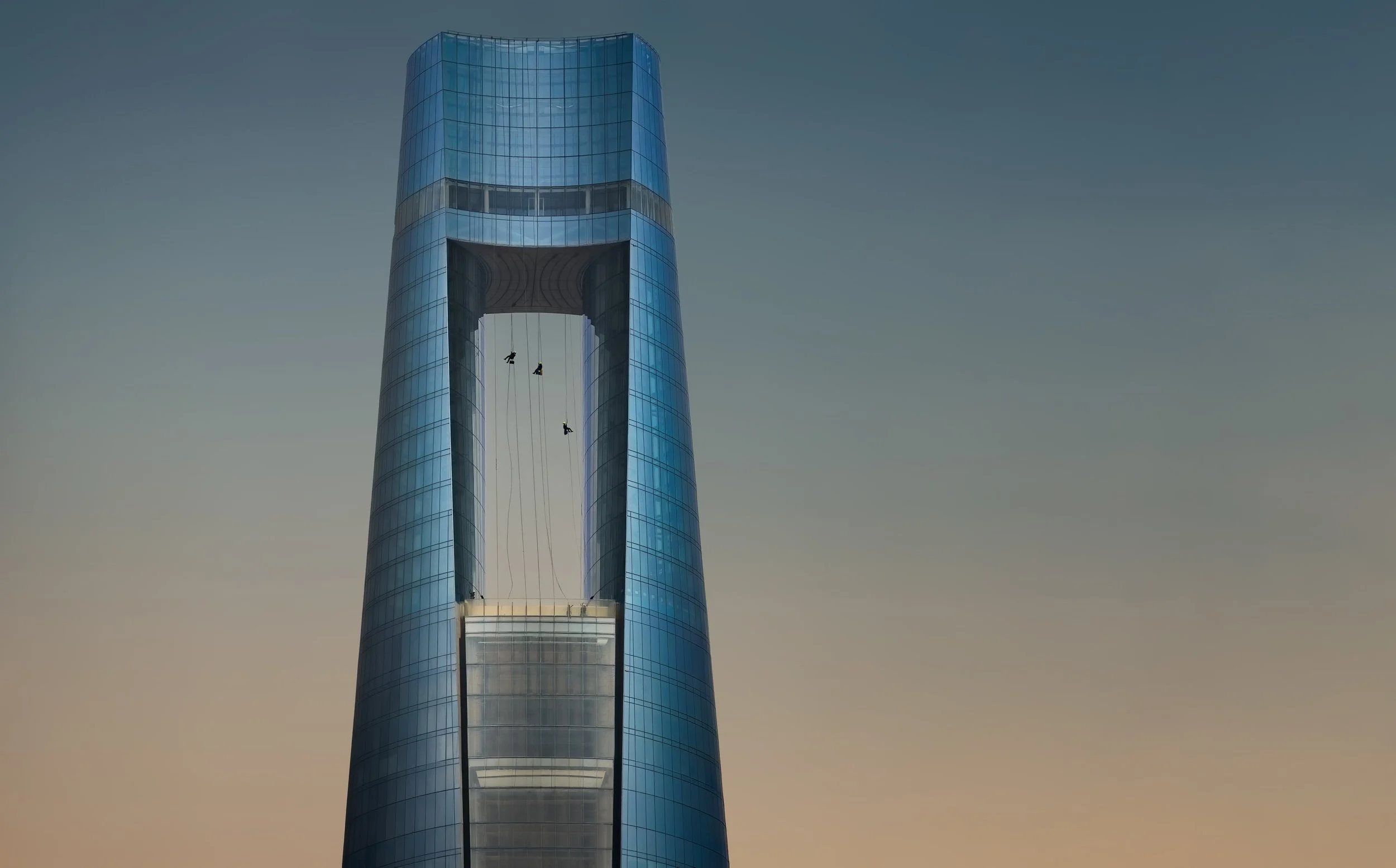 Rope access workers suspended inside the aperture of Ciel Dubai Marina at dusk.