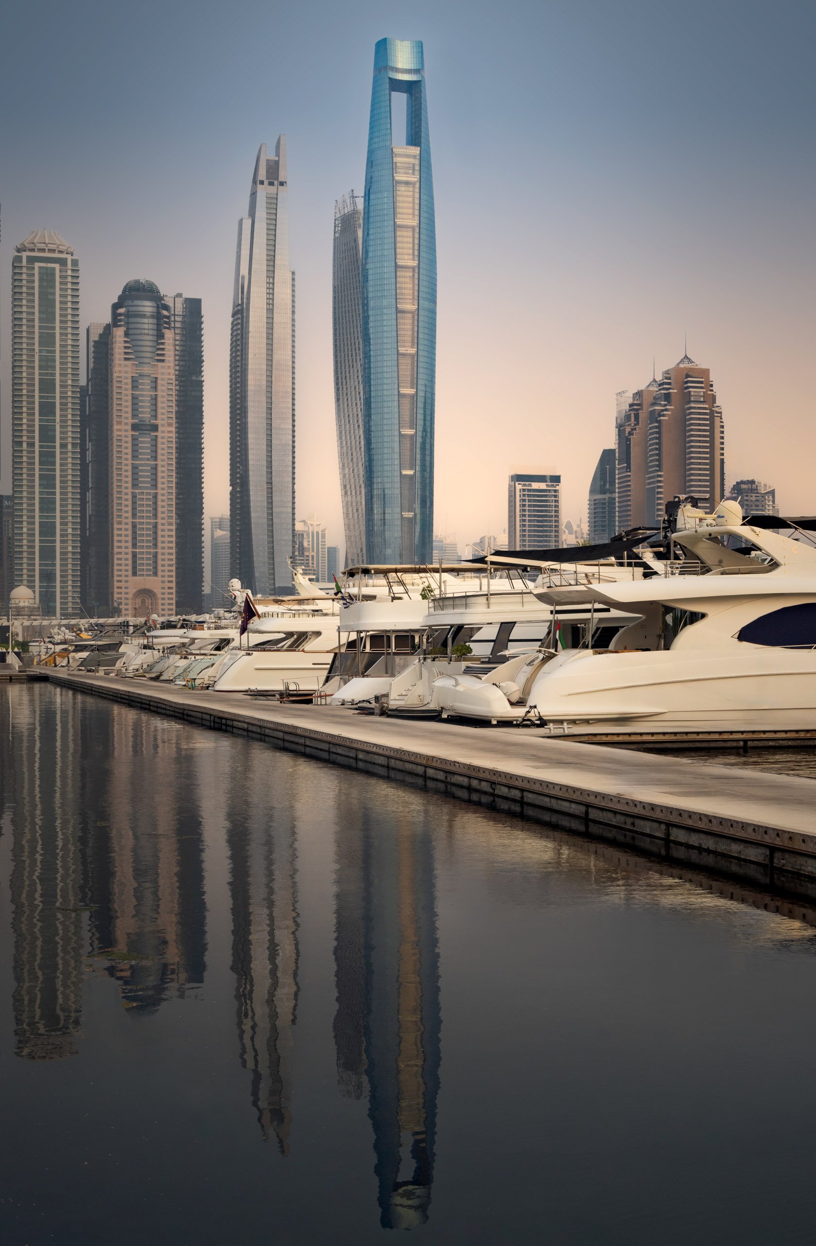Yachts berthed along the marina with Ciel Dubai Marina reflected in the still water.