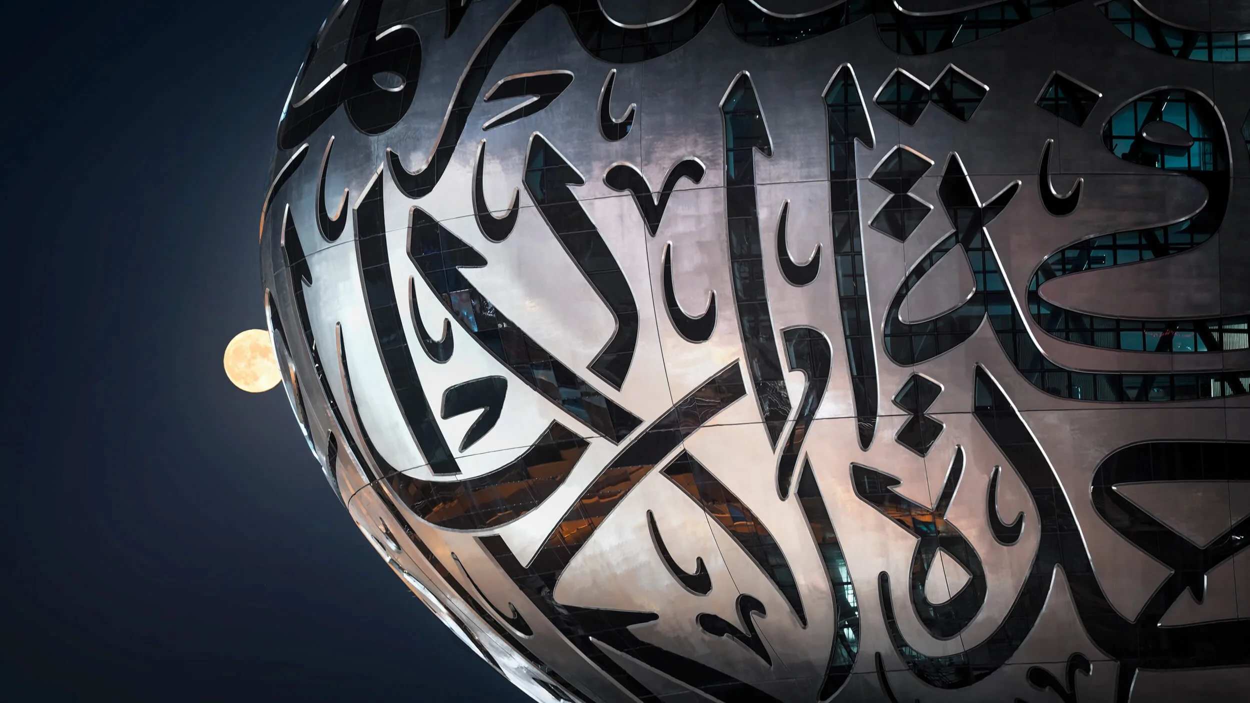 Close-up of a Museum of the Future (MOTF) facade and Arabic calligraphy, moon visible in the night sky in the background- fine art architectural photograph by Ahmad Alnaji, SARAB Art Production