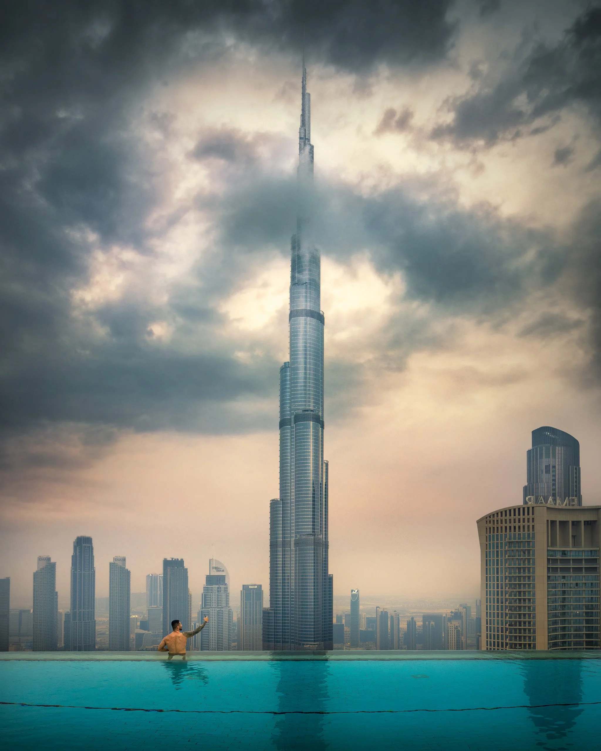 A person in the address skyviews pool. with the Burj Khalifa and Dubai skyline in the background on a cloudy day - fine art drone photograph by Ahmad Alnaji, SARAB Art Production