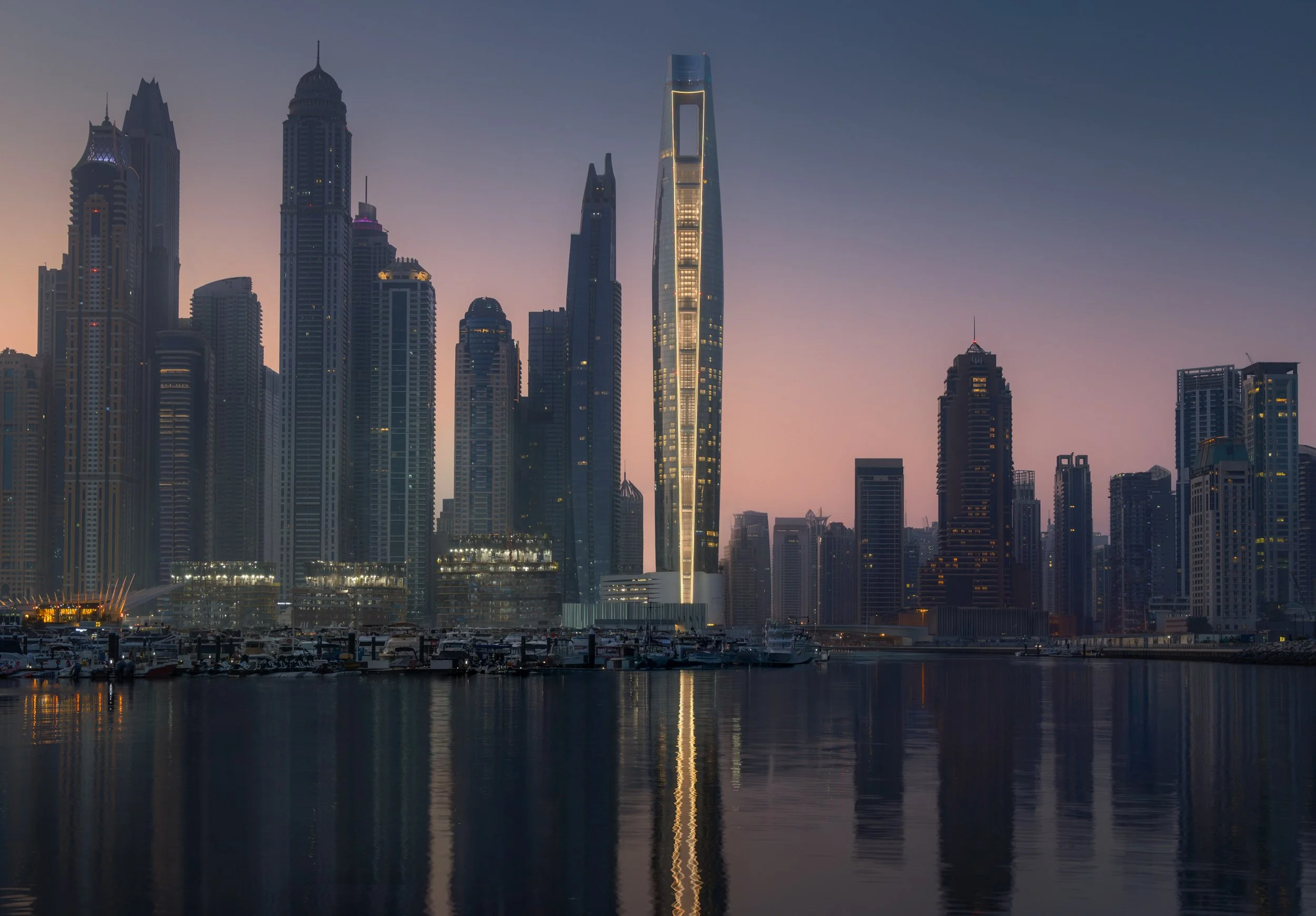 Ciel Dubai Marina by NORR lit at blue hour, the tower reflected in the water of the marina.