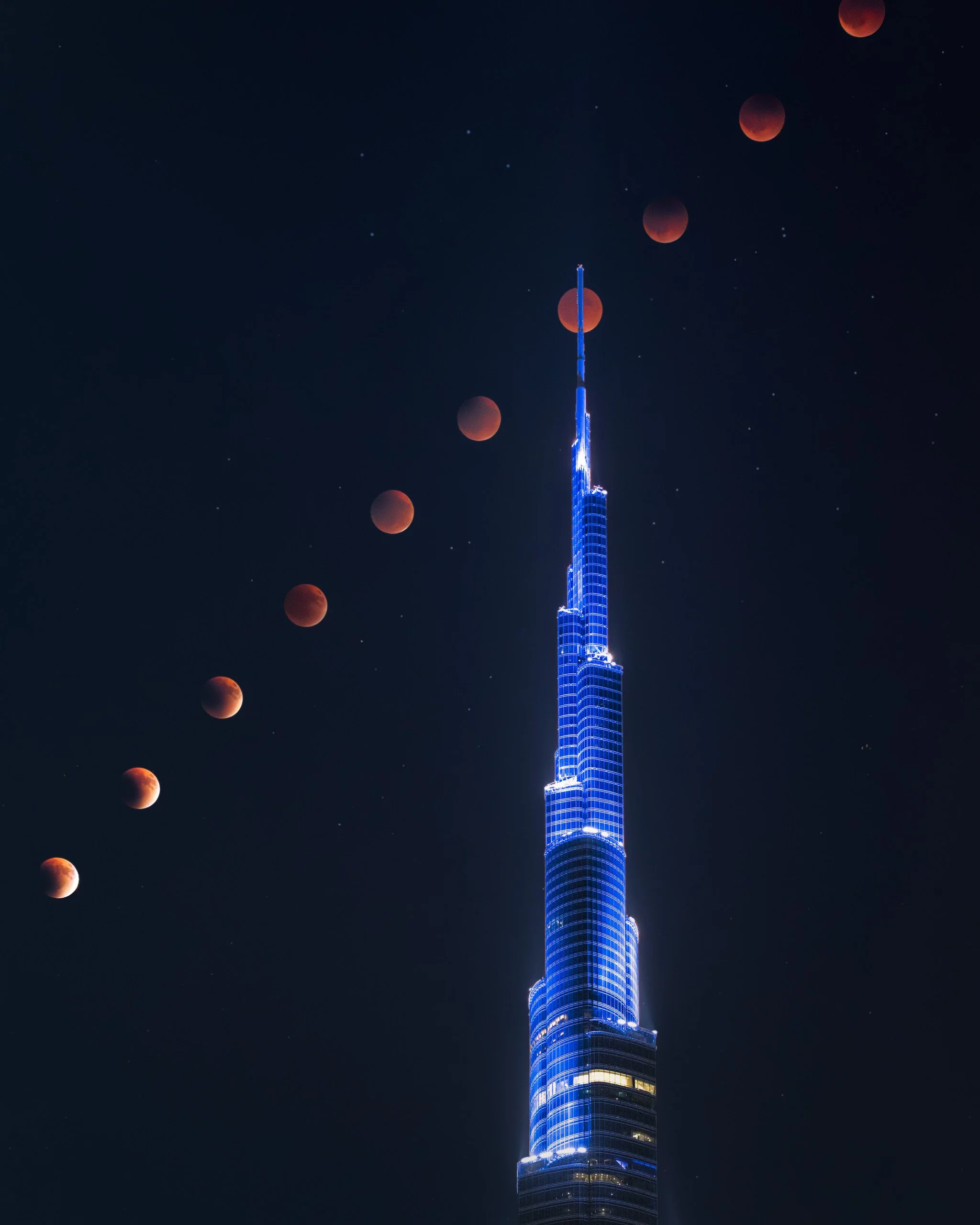 Night sky with stars and different stages of a lunar eclipse, along with Burj Khalifa in Dubai - fine art photograph by Ahmad Alnaji, SARAB Art Production