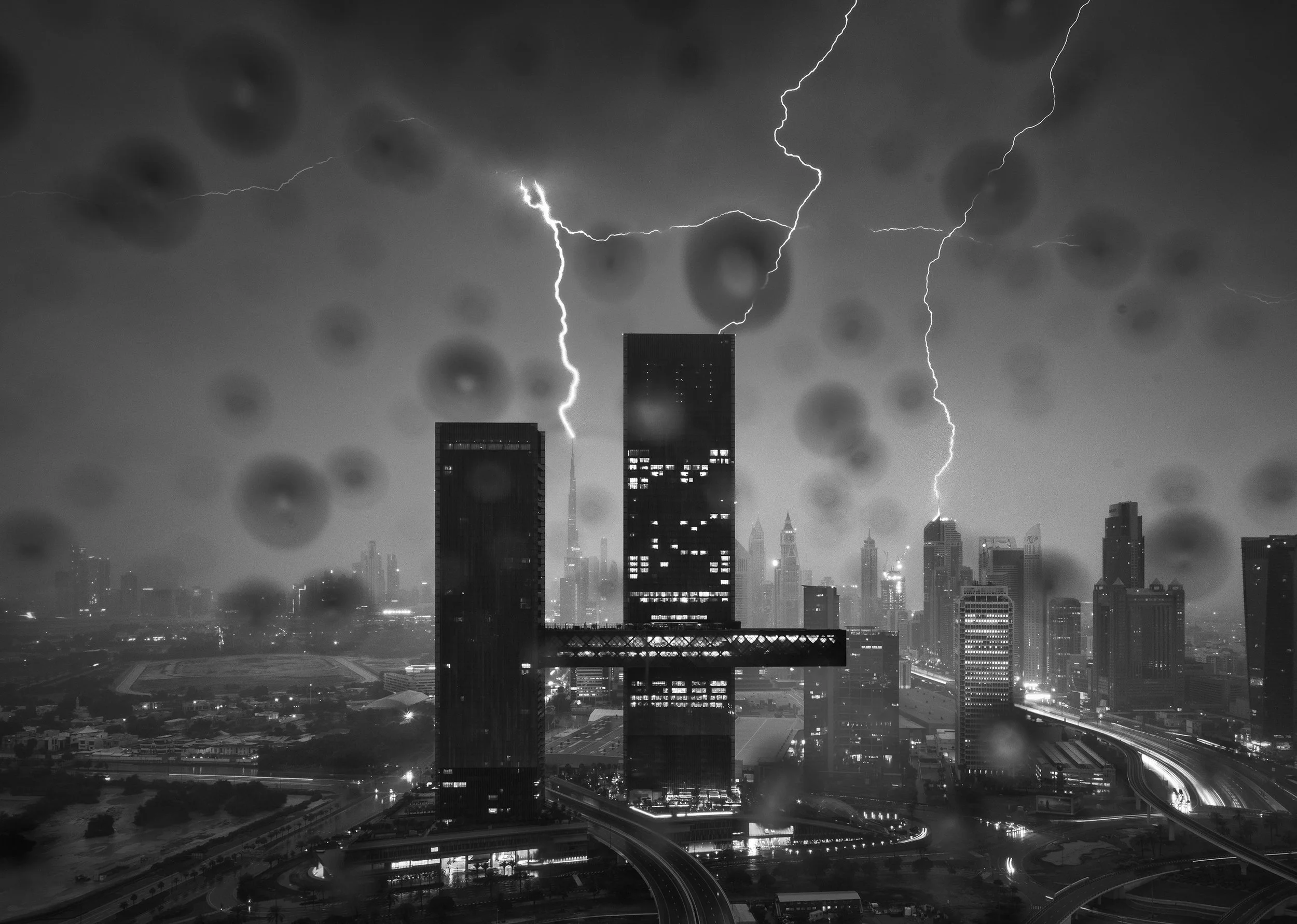 Moody black and white cityscape photography looking through rain-streaked glass at a lightning storm over One Za'abeel (Nikken Sekkei) and Dubai Skyline - A dramatic capture by Ahmad Alnaji, SARAB.