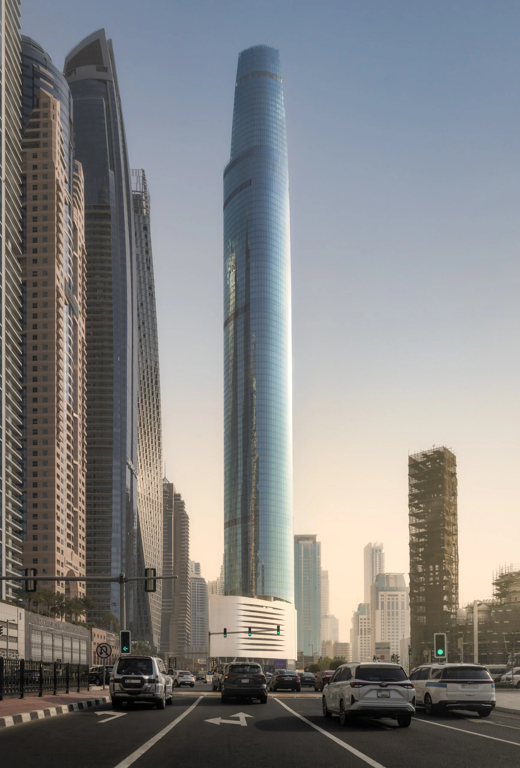 Ciel Dubai Marina rising above a street junction in golden light, traffic waiting at the lights.