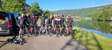 Groep mensen met fietsen op een pad langs een rivier, natuur en bergen op de achtergrond.