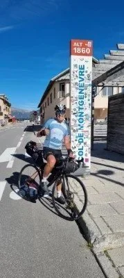 Fietser stopt bij een grenspaal in Genève, met een blauwe lucht op de achtergrond.