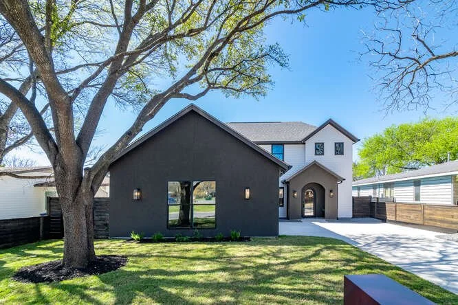 A modern two-story house with white and dark gray siding, a brown roof, and a front porch with an arched entrance.