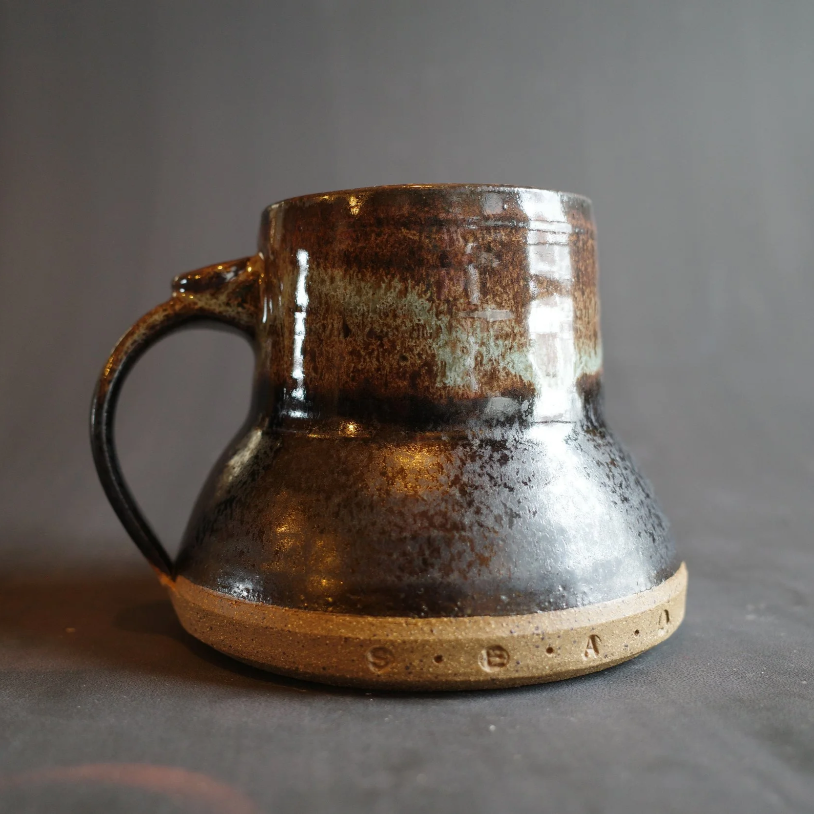 Brown ceramic mug with a handle and a wider bottom