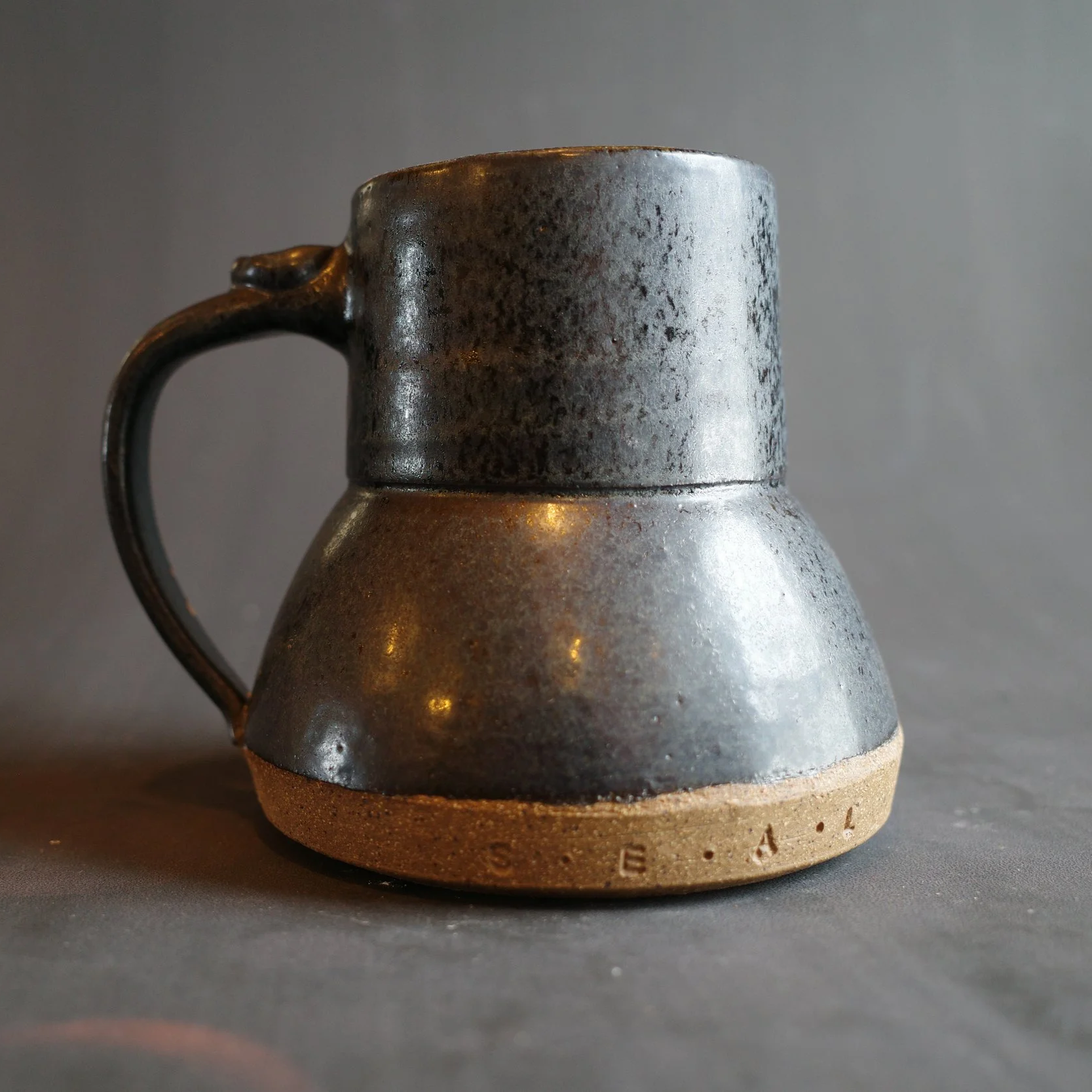 Dark gray ceramic mug with a handle and a wider bottom
