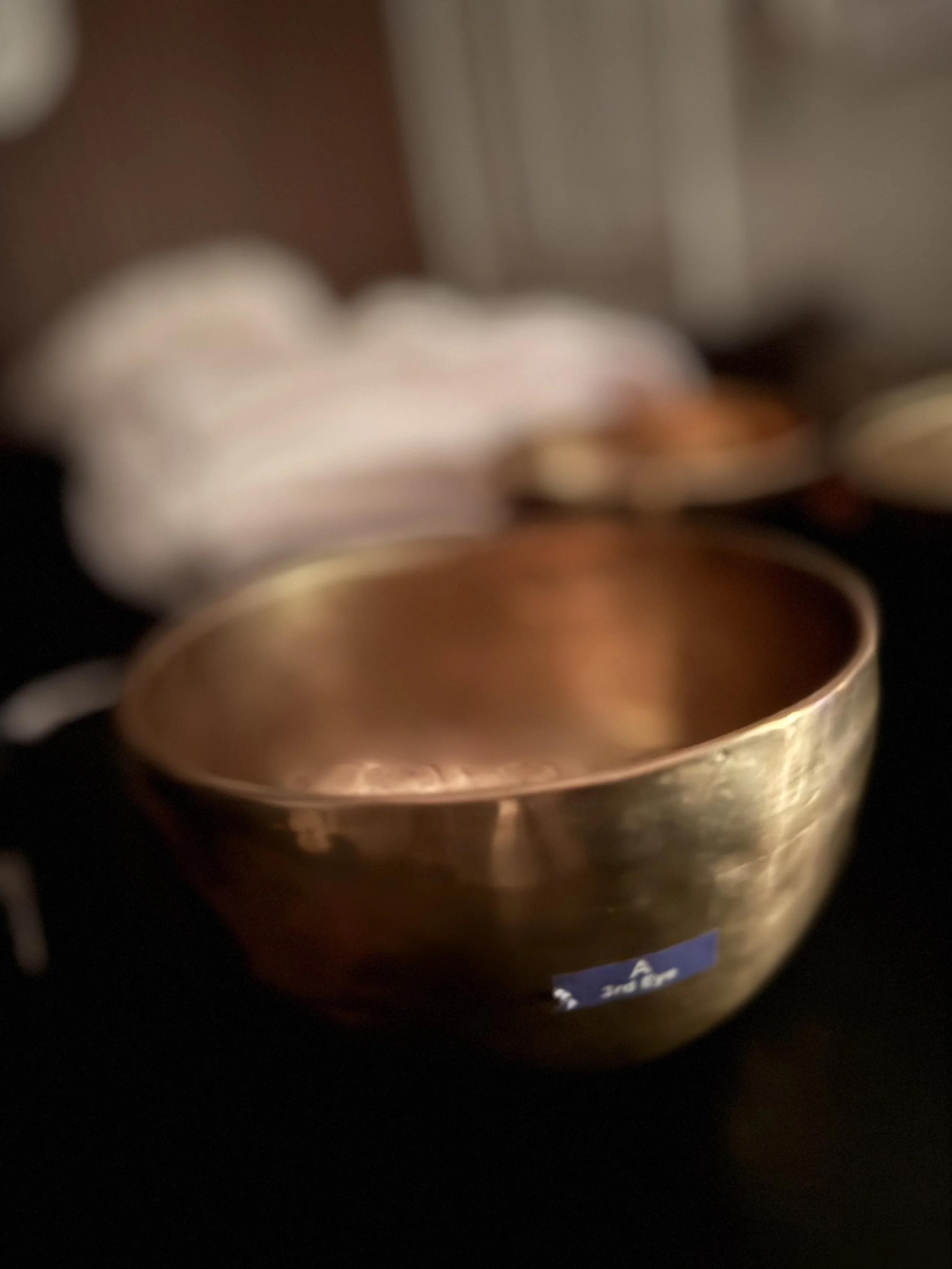 A blurred image of a small copper or bronze bowl with hot liquid inside, set against a dark background.
