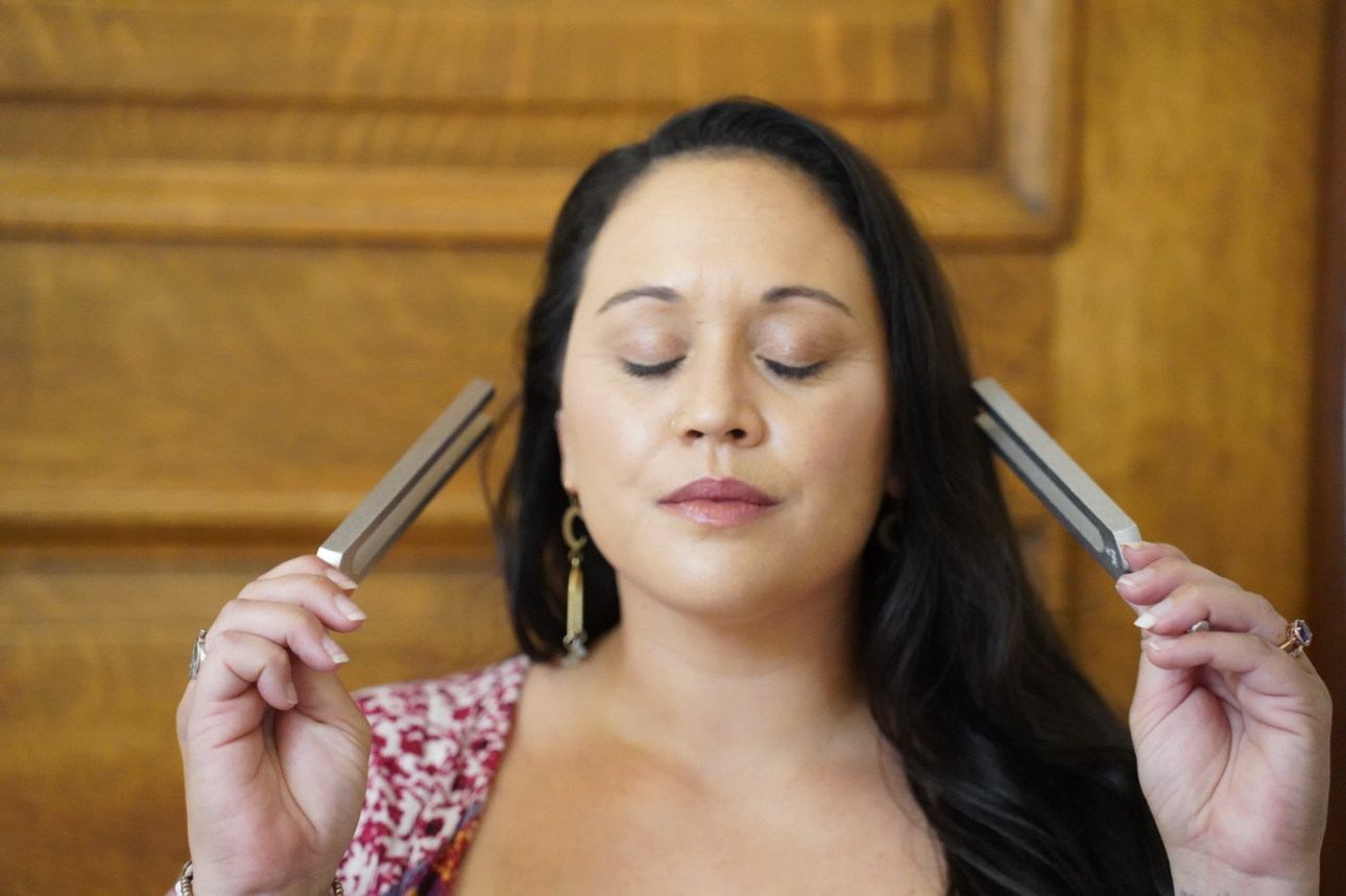 A woman with closed eyes holds two metallic objects near her temples.