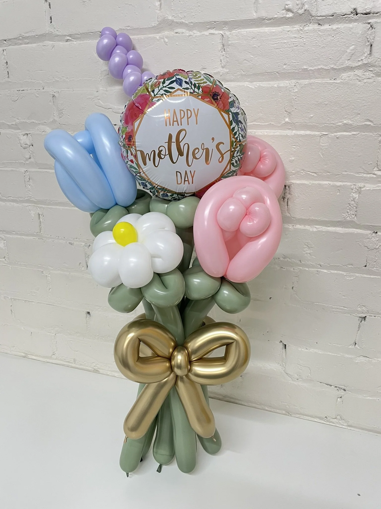 Twisted balloon flowers bundled into a mothers day bouquet with a gold balloon bow on a white background
